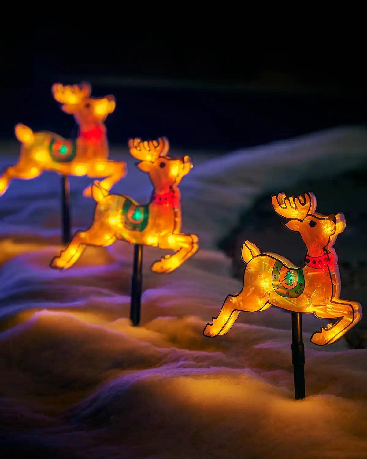 Close-up of three glowing reindeer stake lights arranged in artificial snow