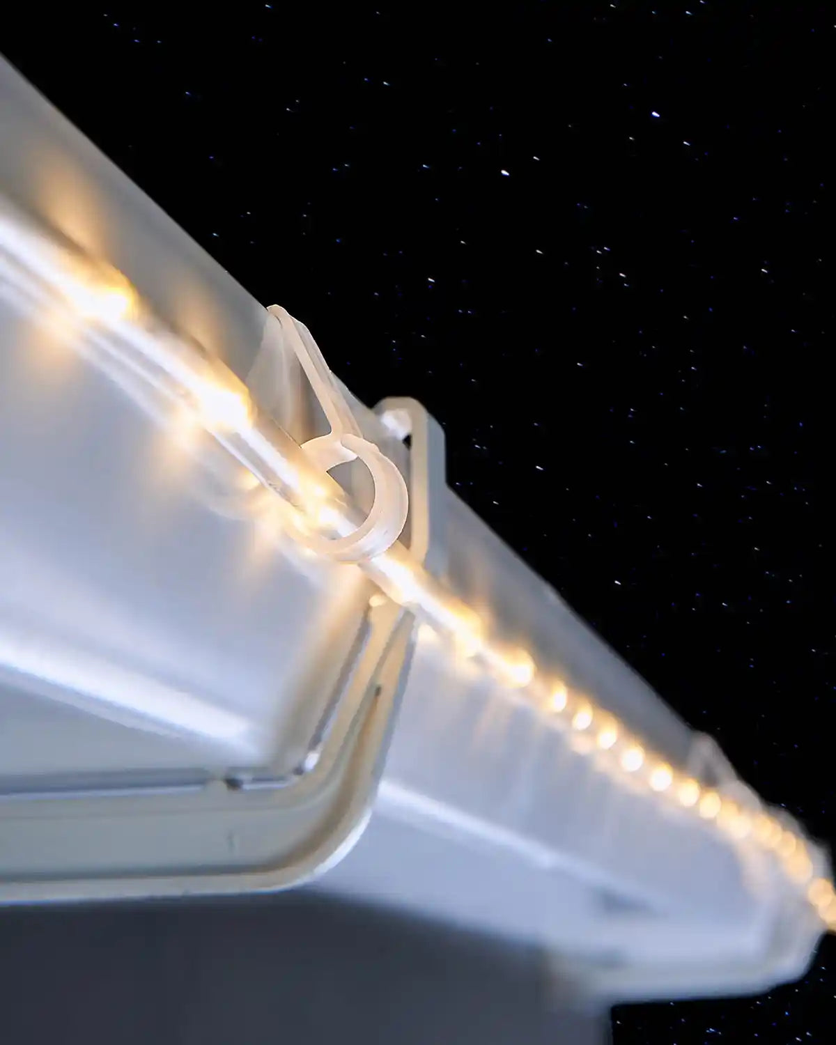 Rope light gutter hook securing warm white Christmas lights along guttering