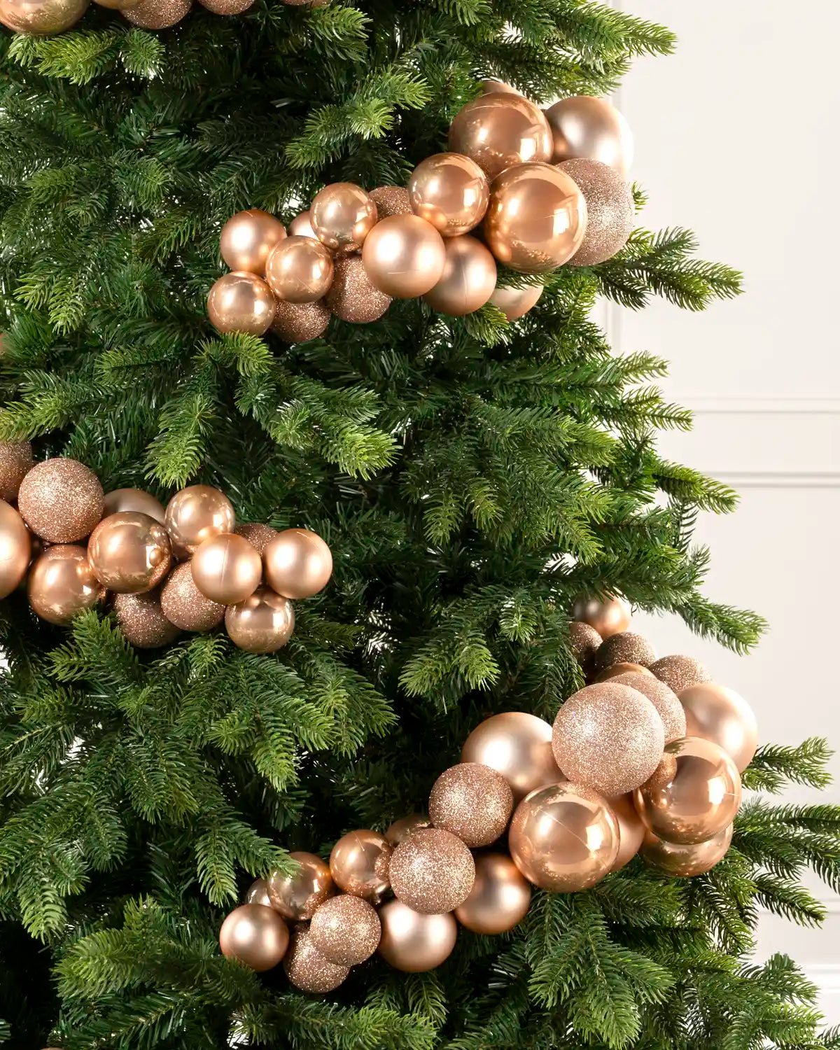 Close-up of rose gold bauble cluster arch on a Christmas tree showing mixed sizes and finishes.