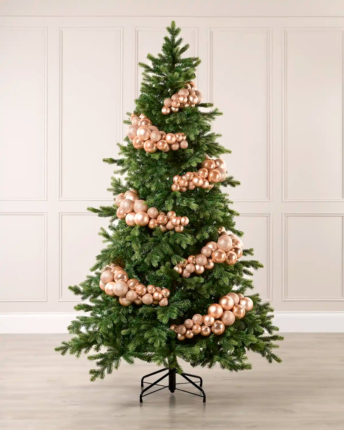 Rose gold bauble cluster arch styled around a green Christmas tree with shiny, matt and glitter baubles.