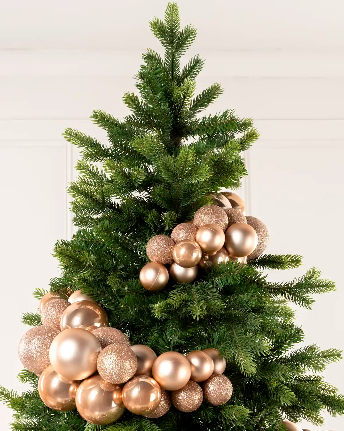 Rose gold bauble cluster arch arranged through the upper branches of a green Christmas tree.