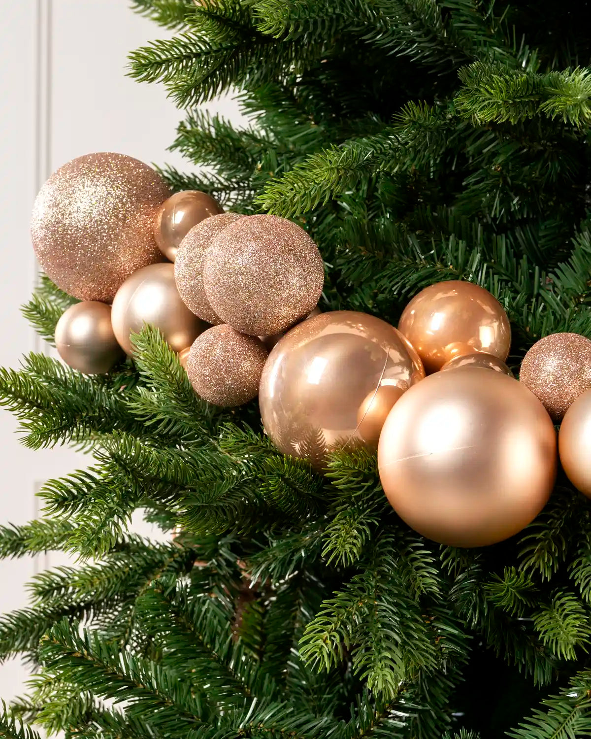 Close-up of rose gold bauble garland on a Christmas tree showing mixed sizes, matt, shiny and glitter finishes.