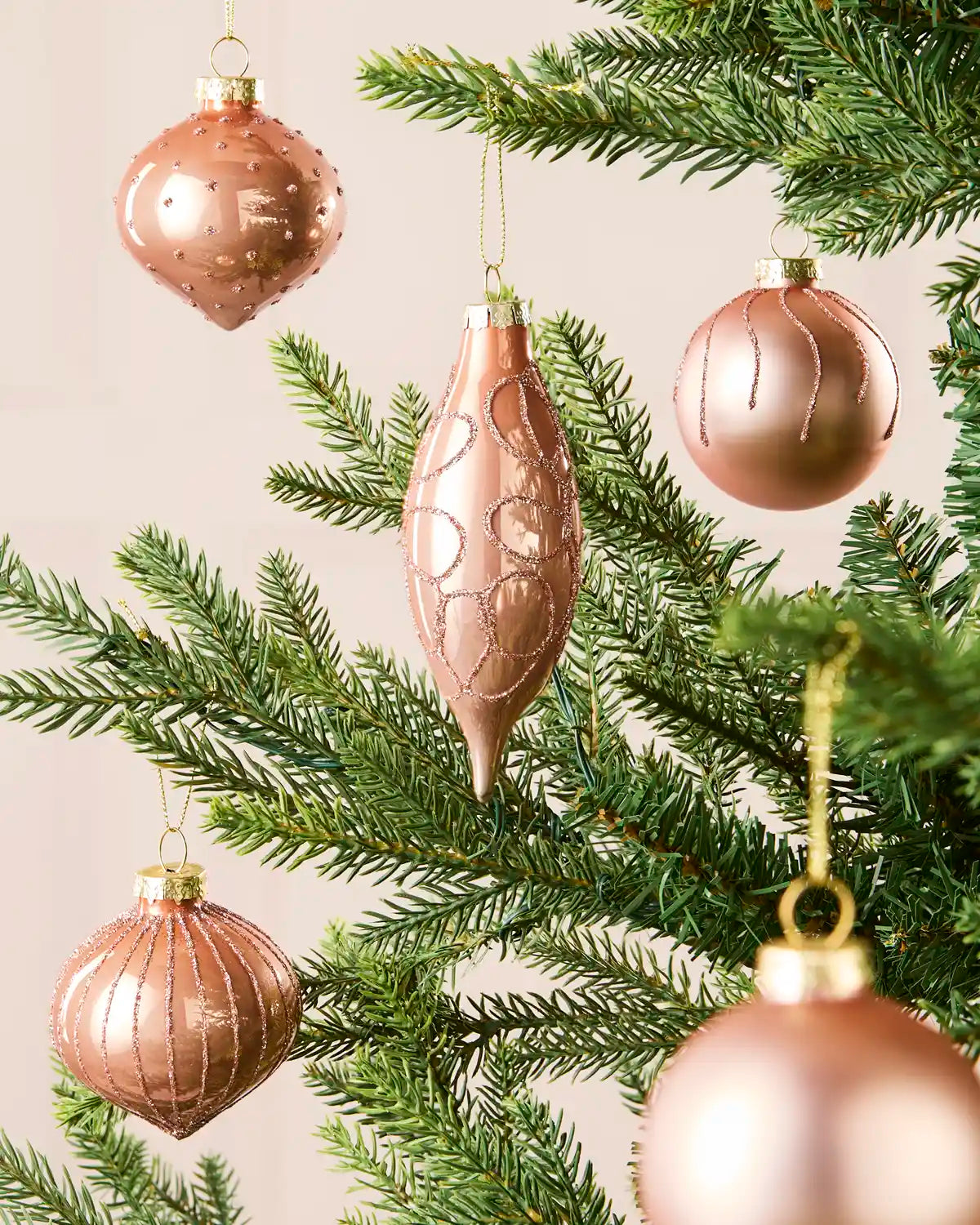 Mixed rose gold glass baubles with matt, shiny and glitter finishes on a Christmas tree.