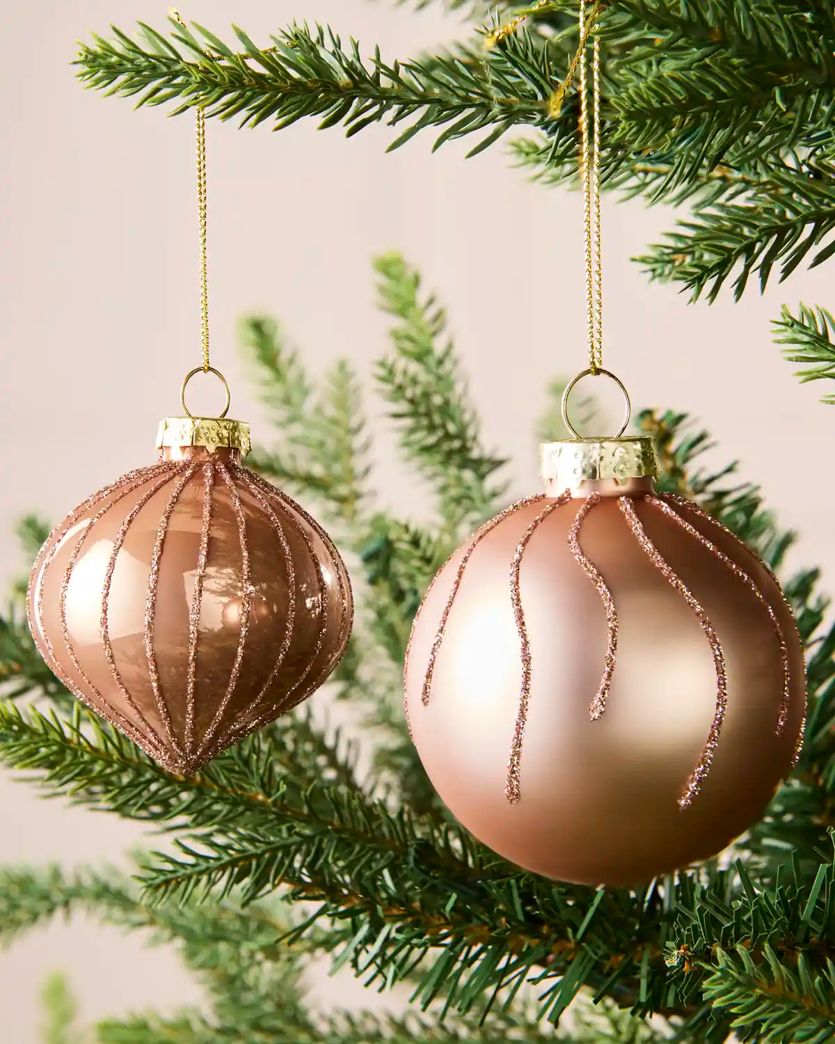 Close-up of rose gold onion-shaped and round glass baubles with glitter stripe patterns.