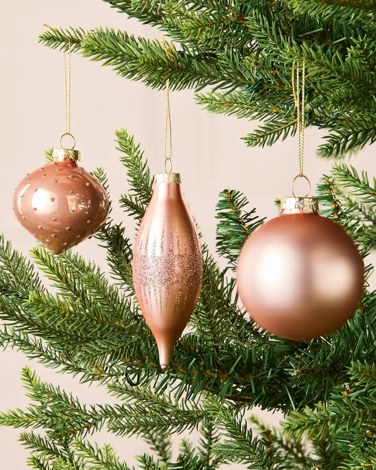 Rose gold round, onion-shaped and teardrop glass baubles displayed on a Christmas tree.