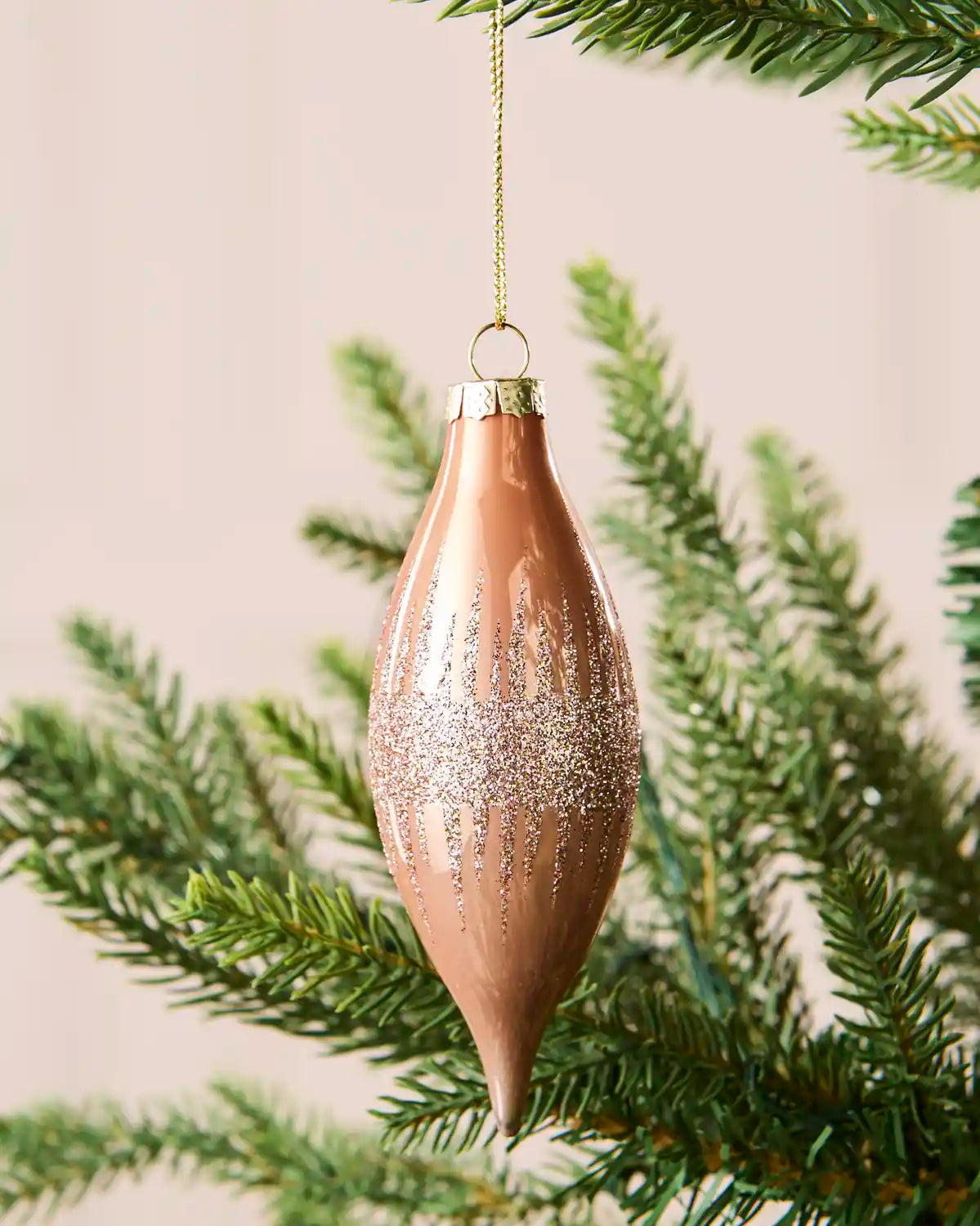 Close-up of a rose gold teardrop glass bauble with glitter lines and a central glitter band.