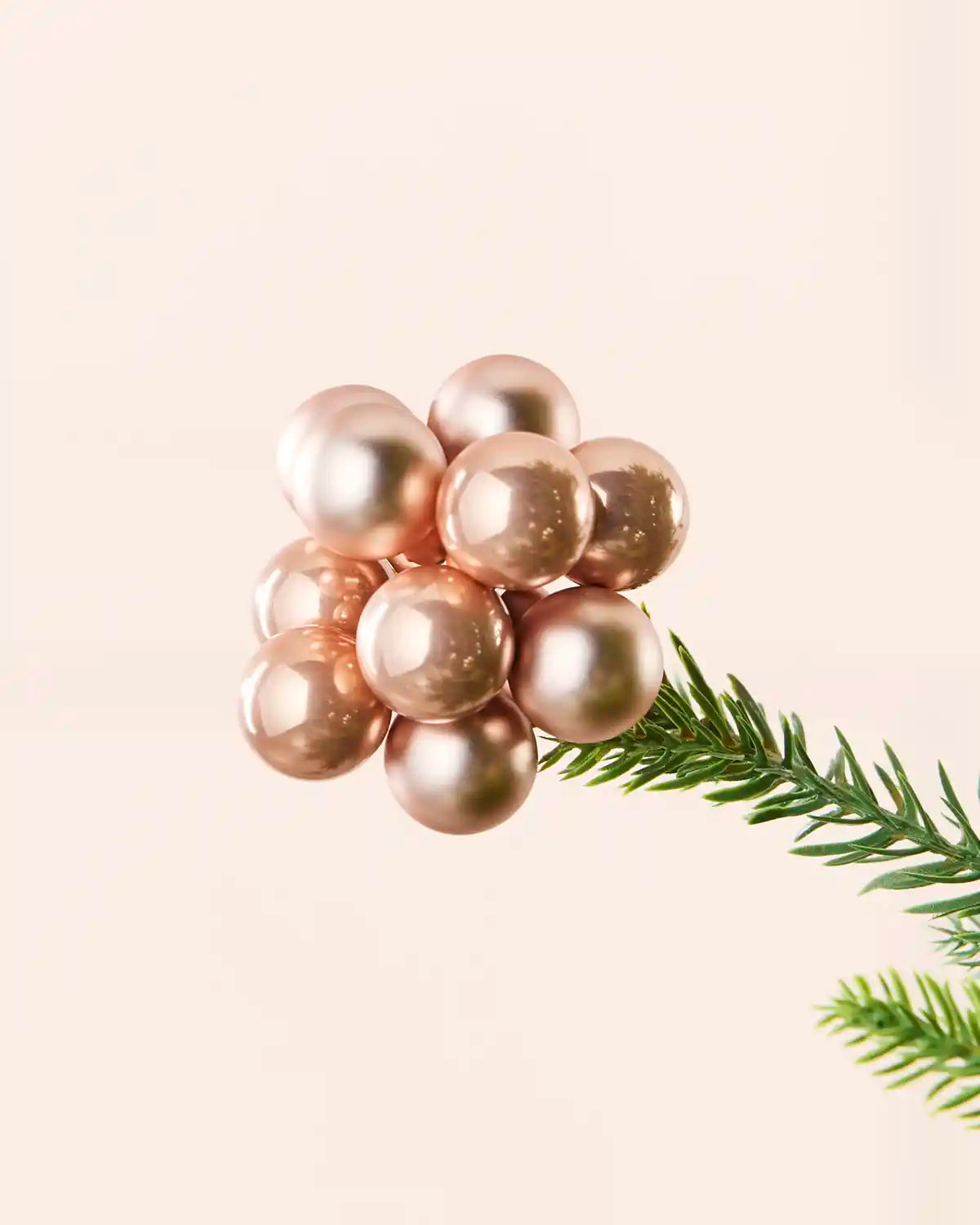 Close-up of a rose gold glass berry cluster bauble attached to a Christmas tree branch.