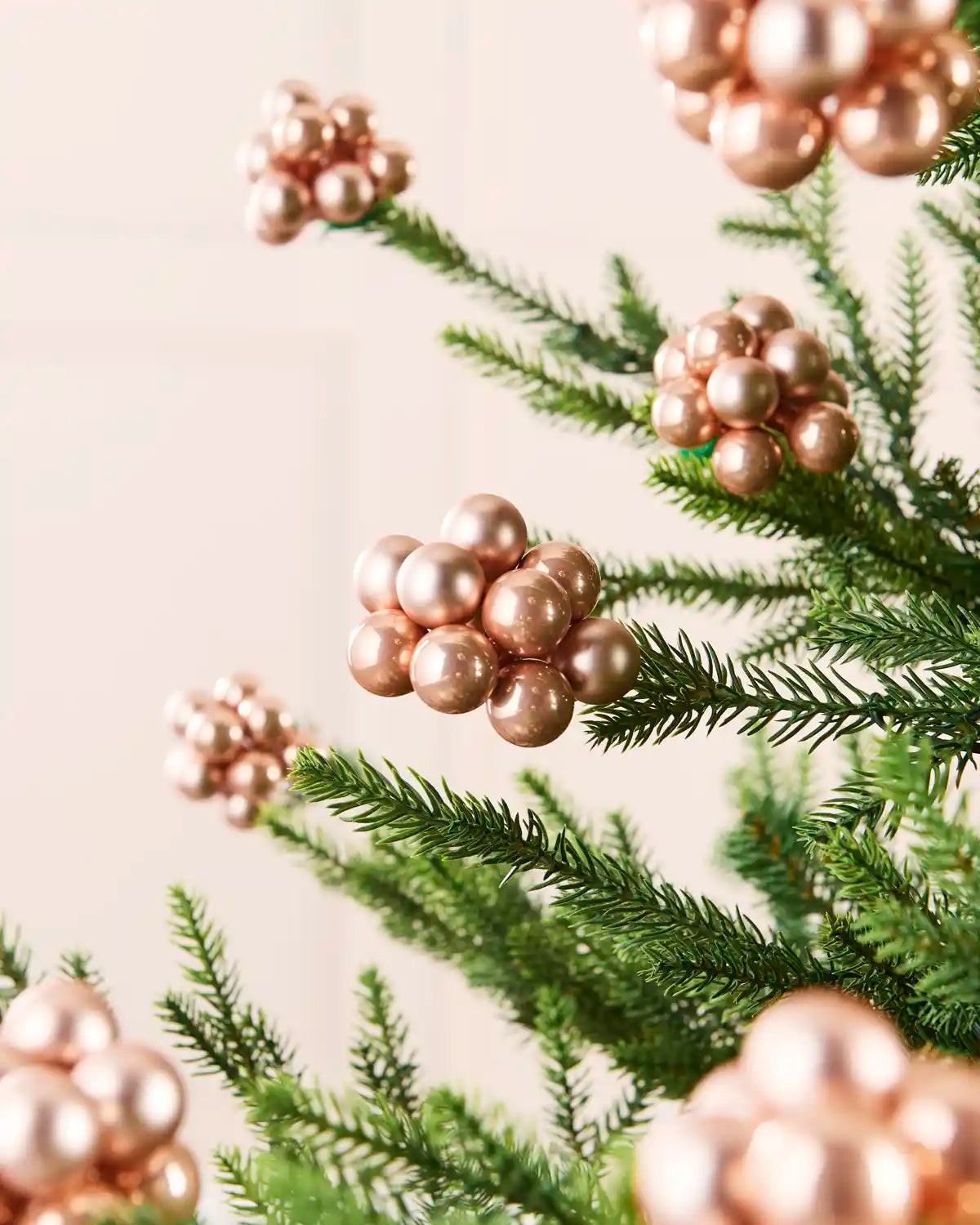 Rose gold glass berry cluster baubles arranged throughout a green Christmas tree.