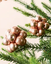 Close-up of rose gold glass berry cluster baubles with shiny and matt finishes on a Christmas tree.