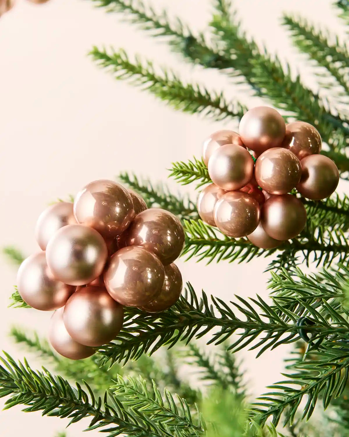 Close-up of rose gold glass berry cluster baubles with shiny and matt finishes on a Christmas tree.