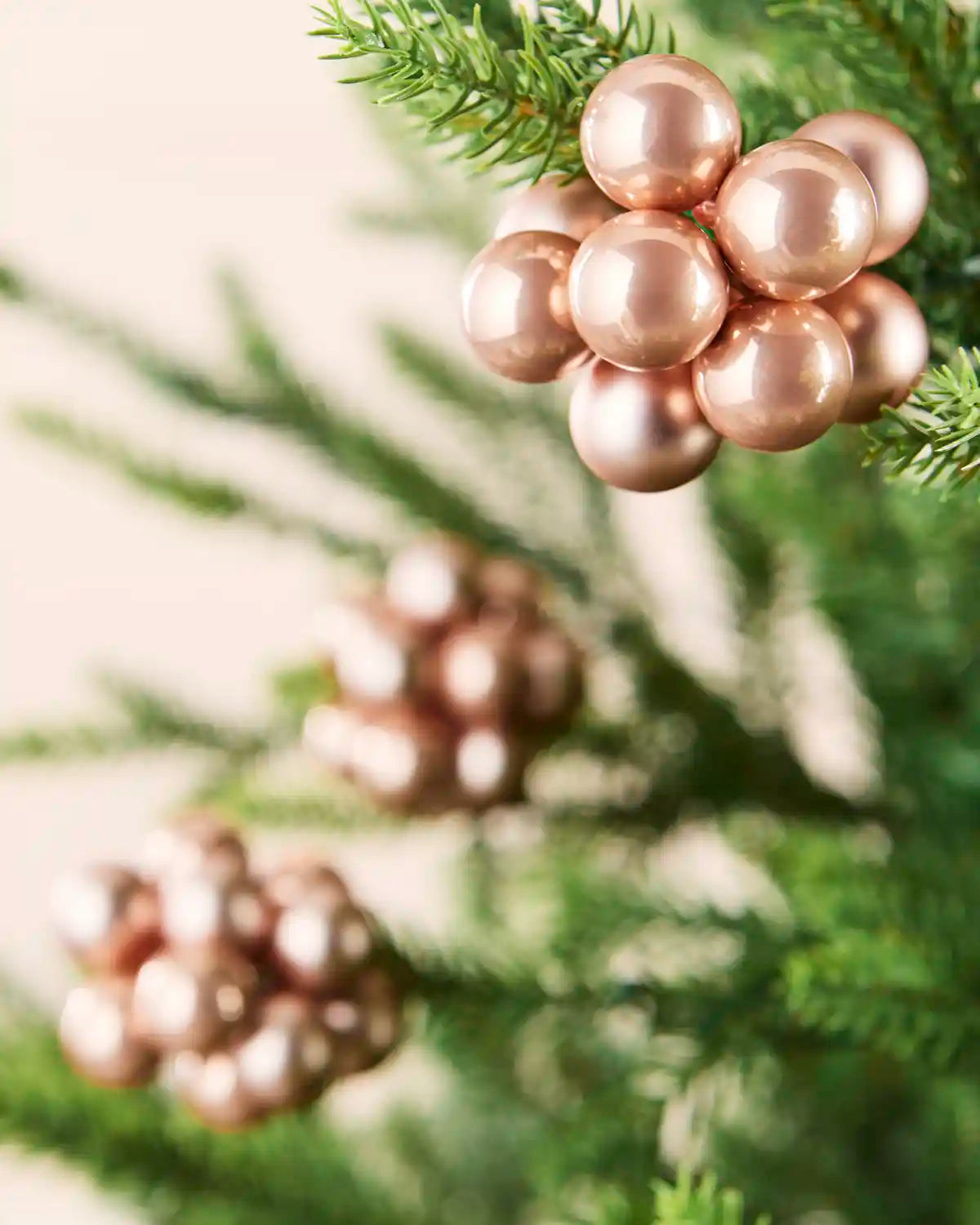 Rose gold berry cluster baubles with mixed shiny and matt glass finishes displayed on Christmas branches.