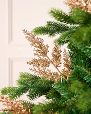Rose gold glitter leaf pick arranged amongst green Christmas tree branches.