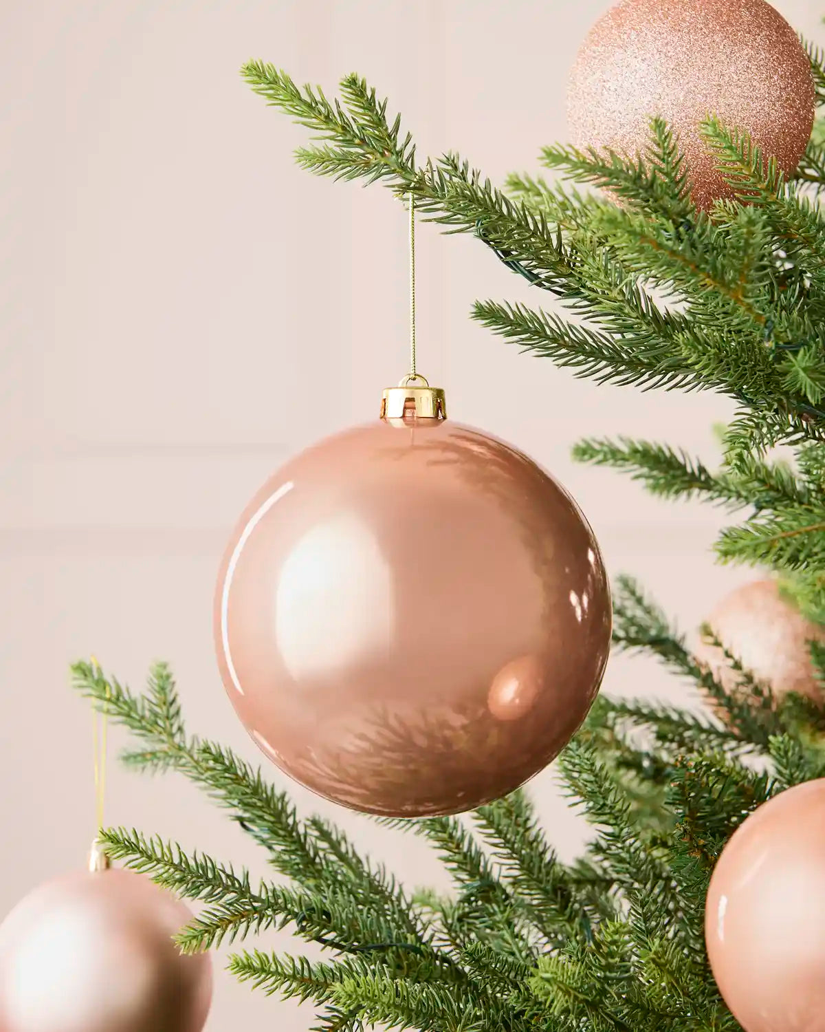 Oversized 15 cm rose gold shiny shatterproof bauble displayed on a Christmas tree with coordinating rose gold baubles.