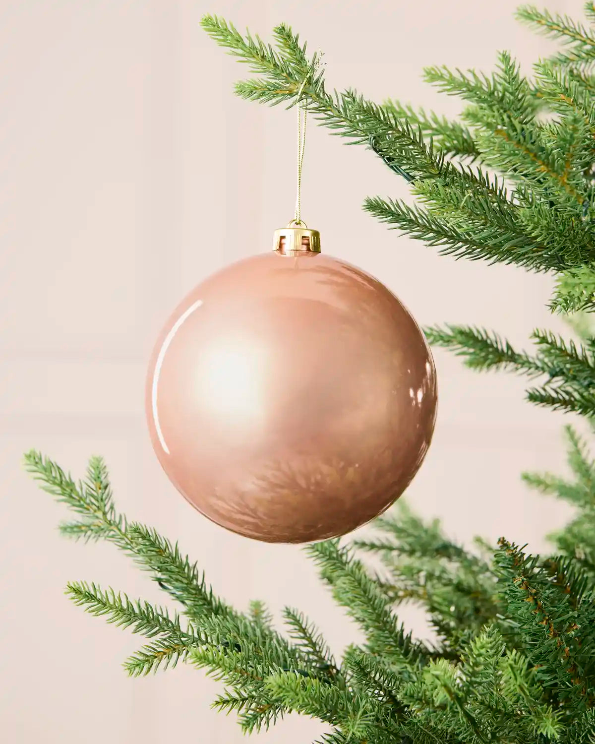 Rose gold 15 cm oversized shatterproof bauble with a shiny finish, gold cap and hanging string displayed on a Christmas tree.