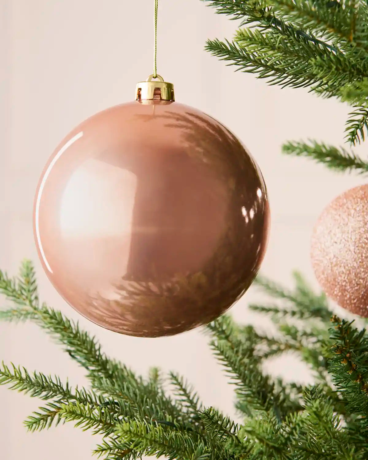 Close-up of a 15 cm oversized rose gold shatterproof bauble with a smooth shiny finish on a Christmas tree.