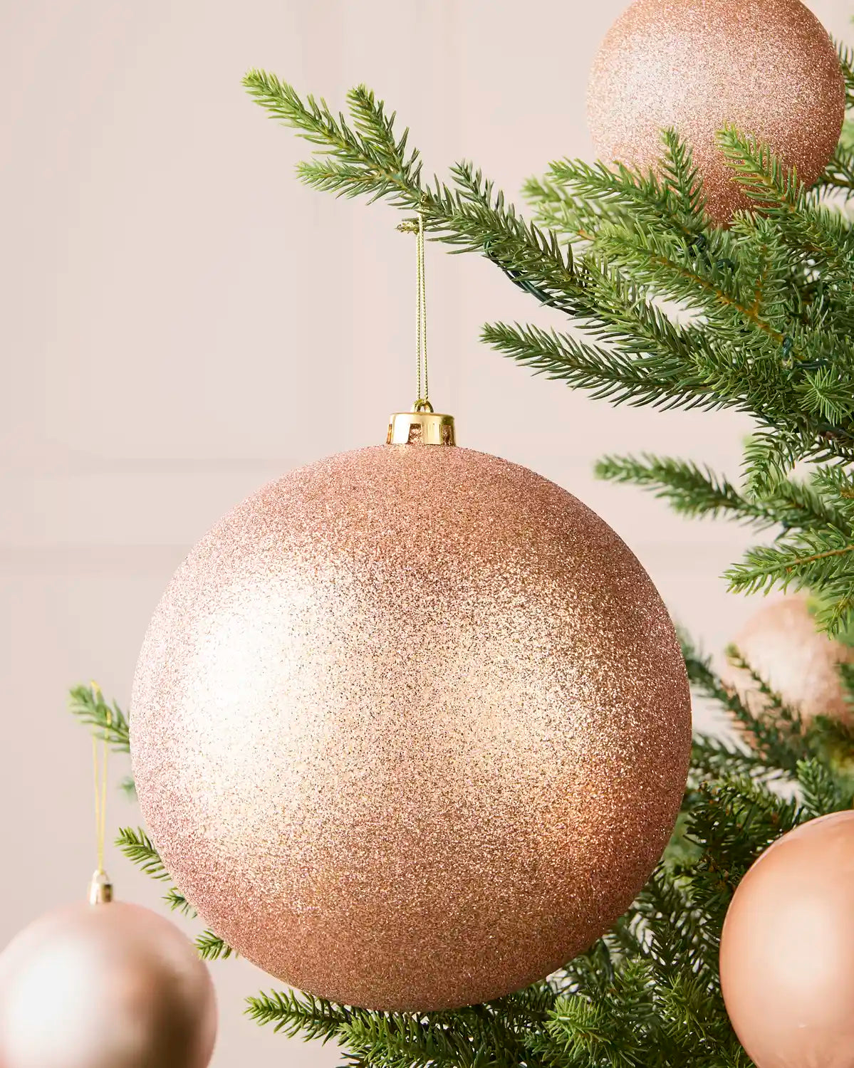 Rose gold 20 cm oversized glitter shatterproof bauble displayed on a Christmas tree with coordinating baubles.