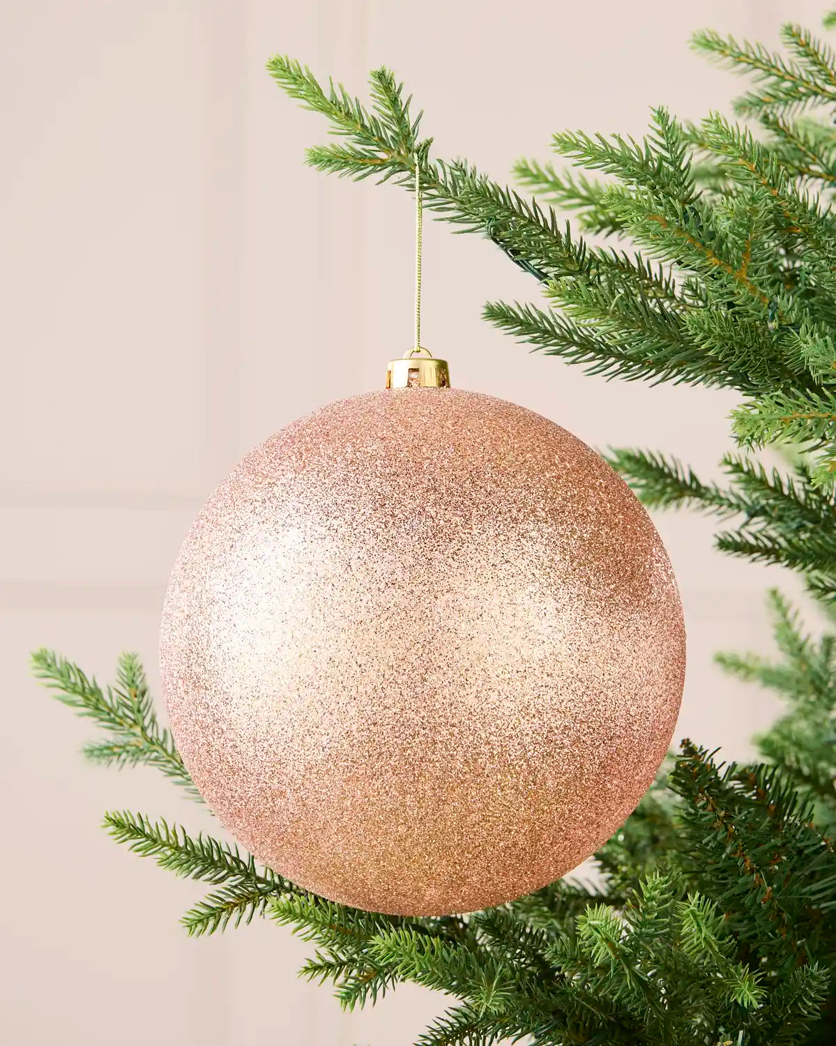 Rose gold 20 cm oversized glitter shatterproof bauble hanging on a Christmas tree with a gold cap and string.