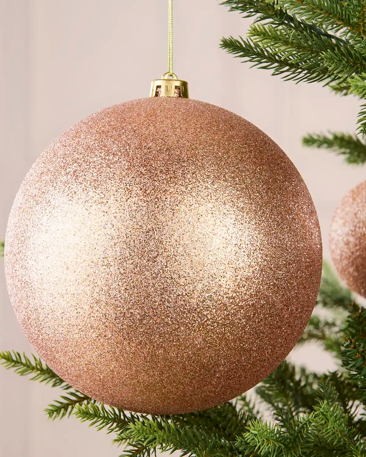 Close-up of a rose gold 20 cm oversized shatterproof bauble with a sparkling glitter finish on a Christmas tree.