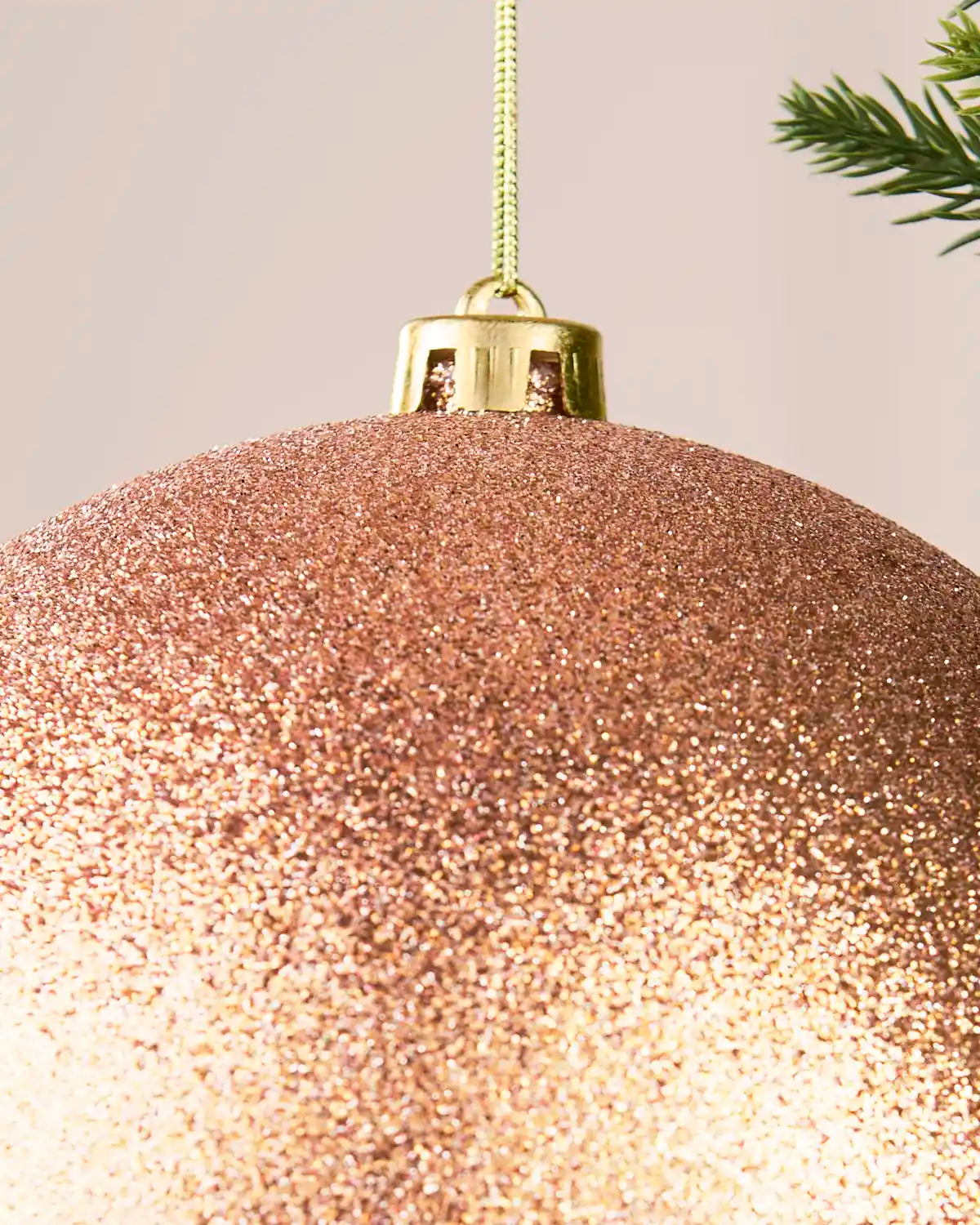 Detail of a rose gold 20 cm oversized glitter shatterproof bauble with gold cap and hanging string.