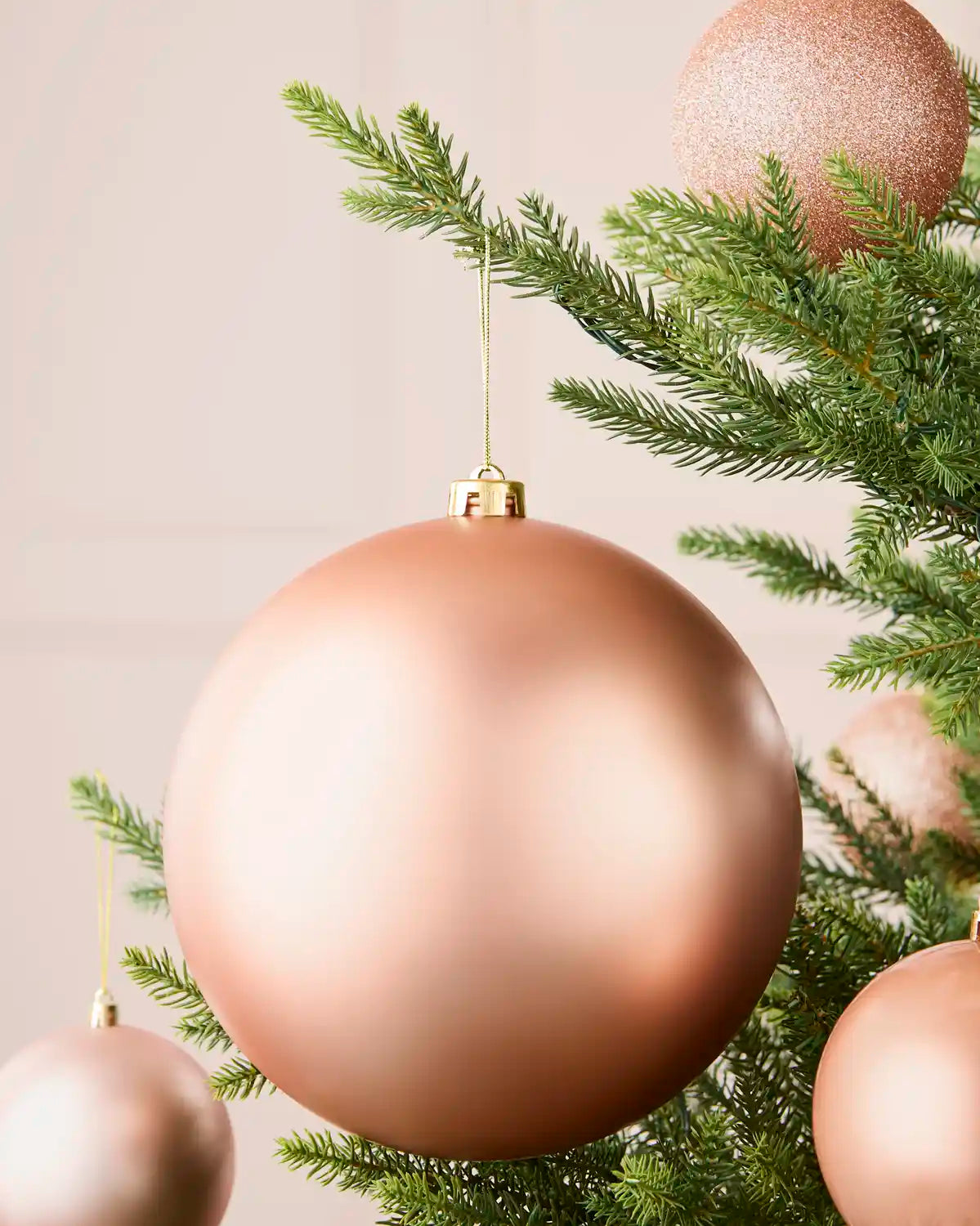 Rose gold 20 cm oversized matt shatterproof bauble displayed on a Christmas tree with coordinating baubles.