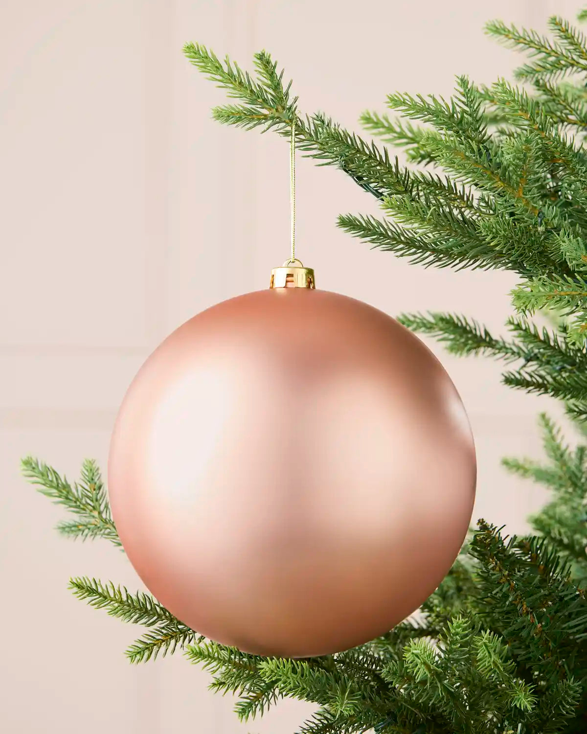 Rose gold 20 cm oversized matt shatterproof bauble hanging on a Christmas tree with a gold cap and string.