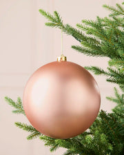 Rose gold 20 cm oversized matt shatterproof bauble hanging on a Christmas tree with a gold cap and string.