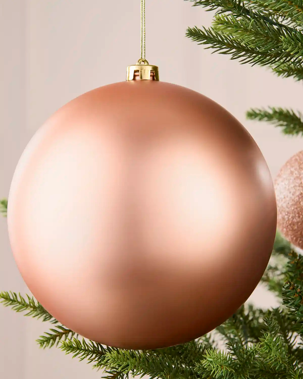 Close-up of a rose gold 20 cm oversized shatterproof bauble with a smooth matt finish on a Christmas tree.