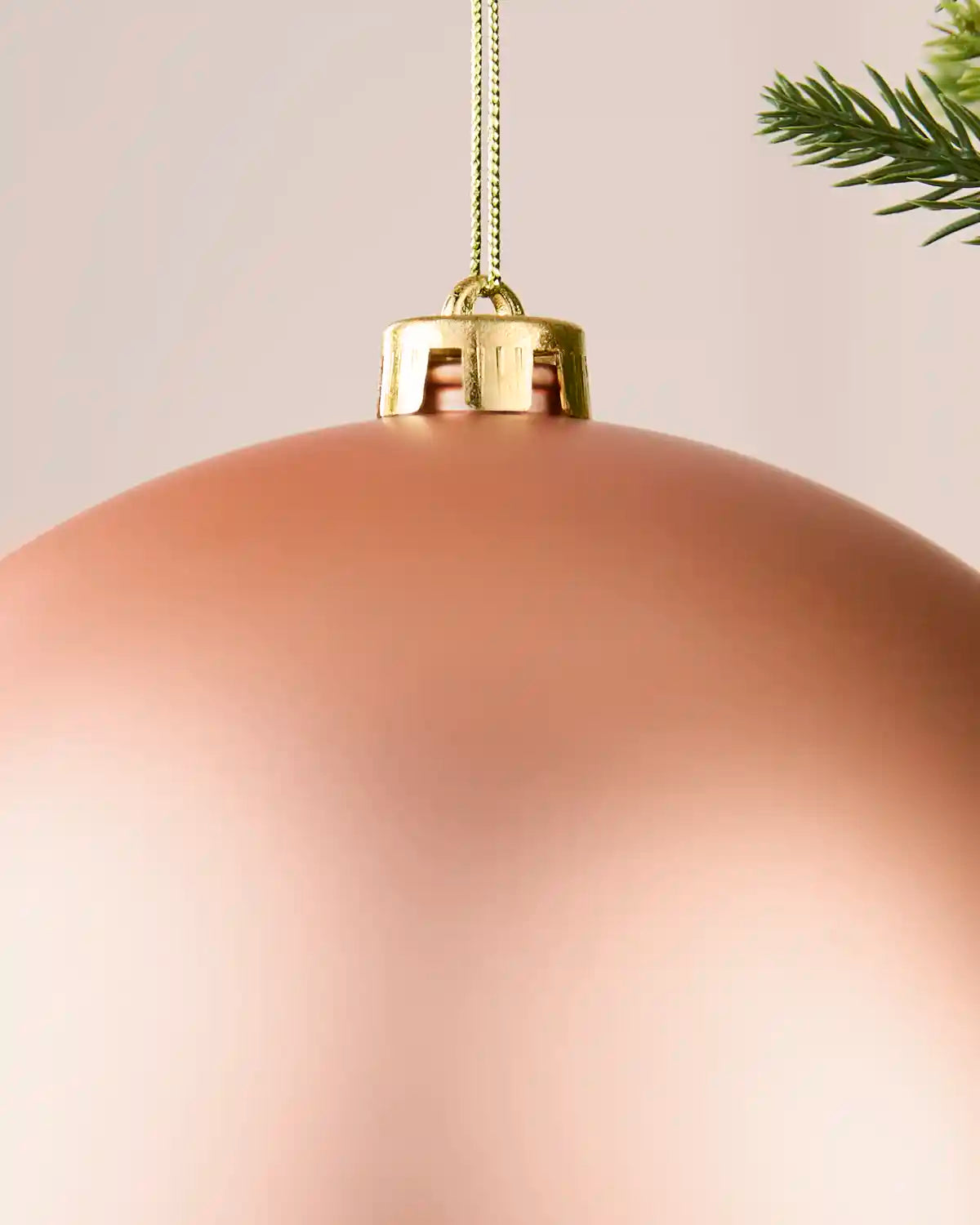 Detail of a rose gold 20 cm oversized matt shatterproof bauble with gold cap and hanging string.