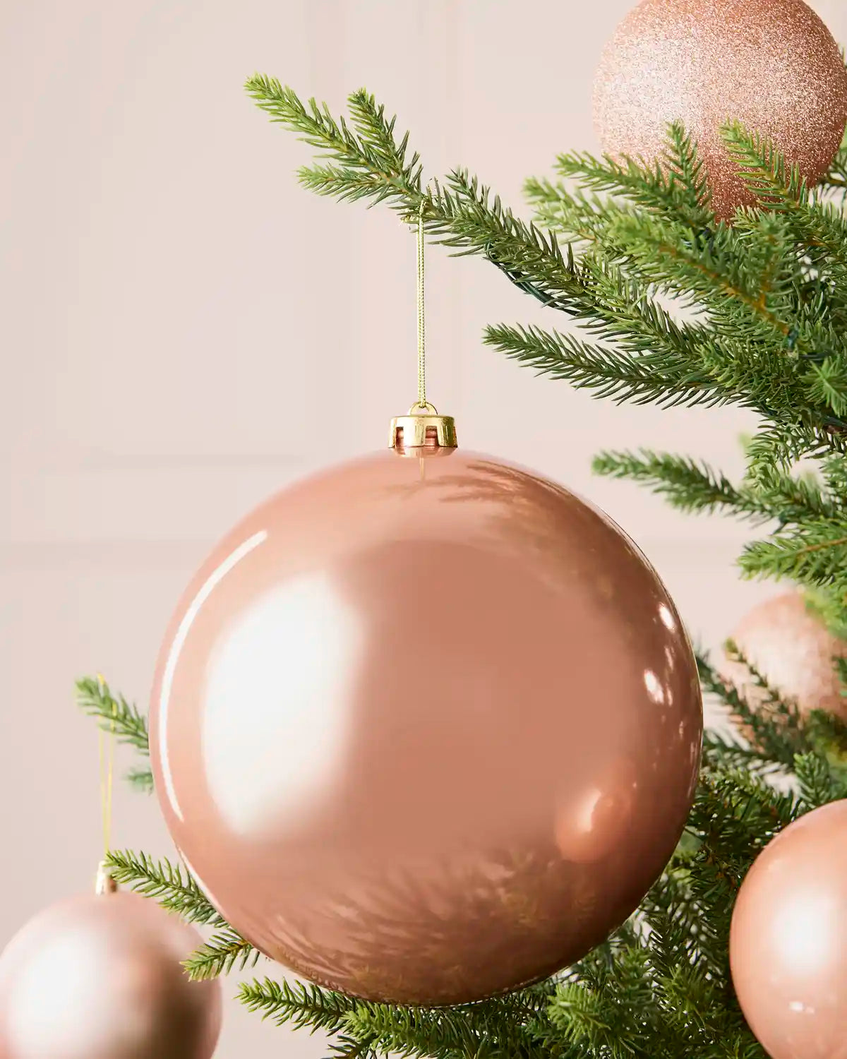 Rose gold 20 cm oversized shiny shatterproof bauble displayed on a Christmas tree with coordinating baubles.