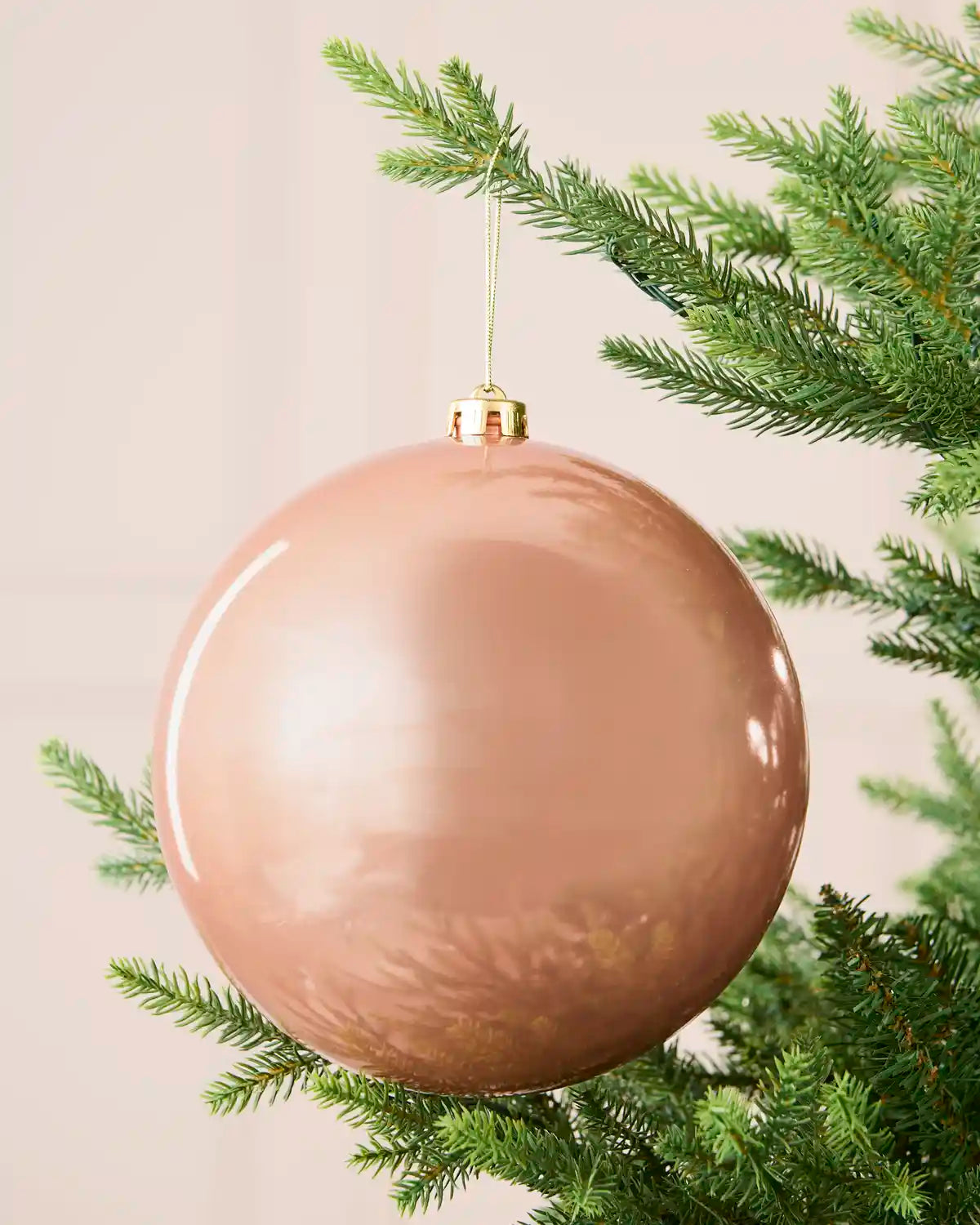 Rose gold oversized shiny shatterproof bauble hanging on a Christmas tree, 20 cm