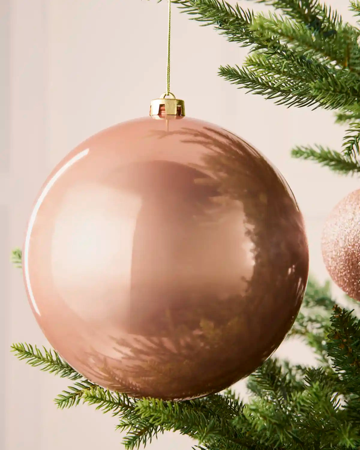 Close-up of a rose gold 20 cm oversized shiny shatterproof bauble hanging on a Christmas tree.