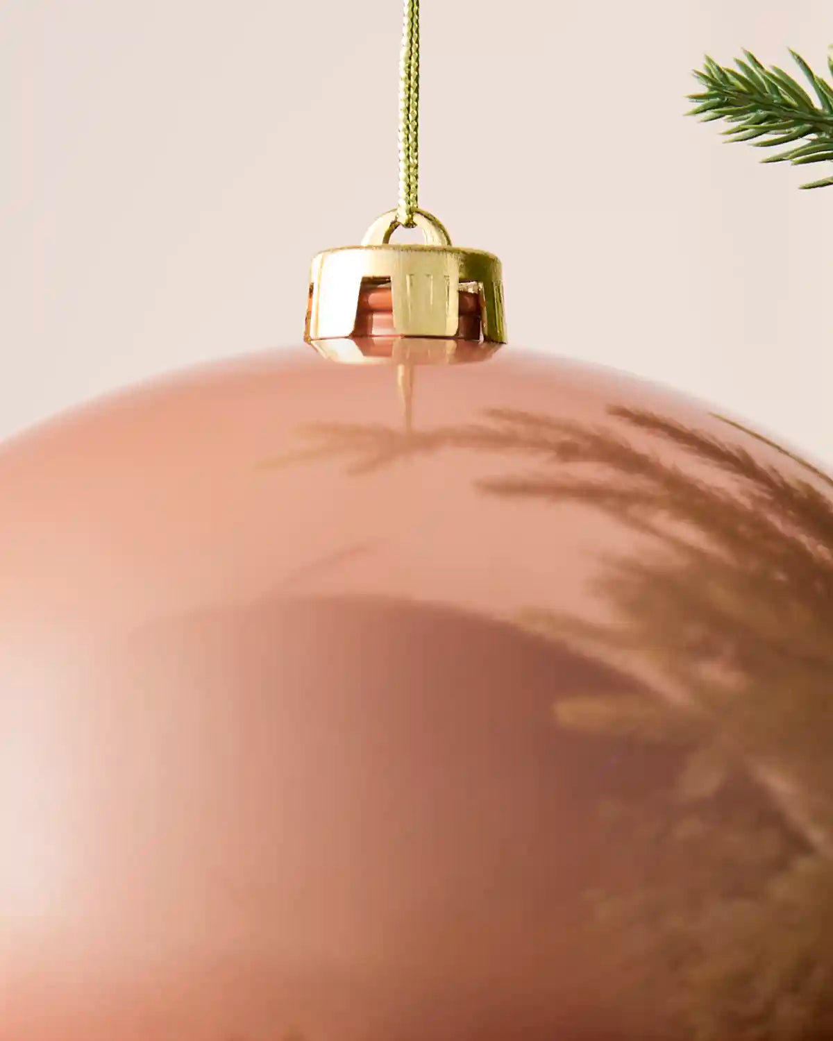 Detail of a rose gold 20 cm oversized shiny shatterproof bauble with gold cap and hanging string.