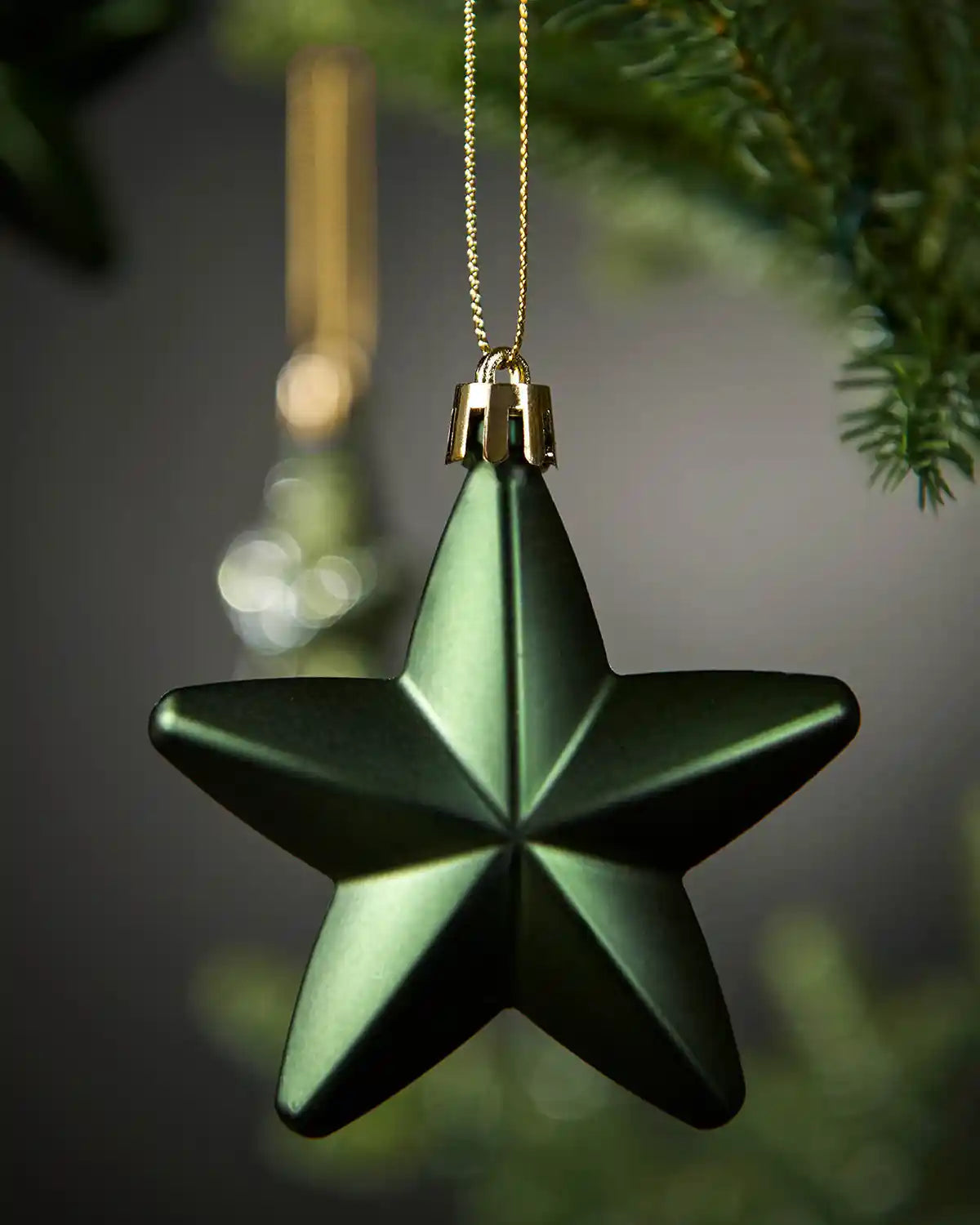 Close-up of a matte sage green 7cm hanging star with gold string.