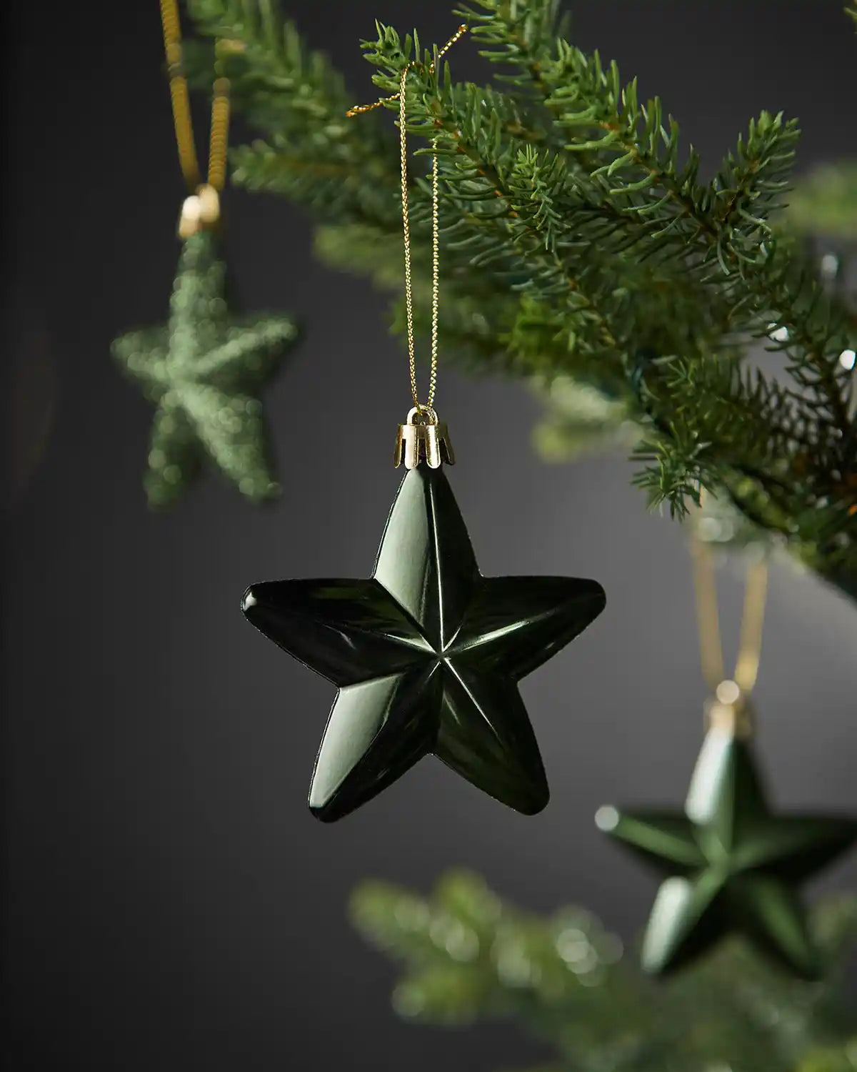 Close-up of a shiny sage green 7cm hanging star with gold string on a Christmas tree.