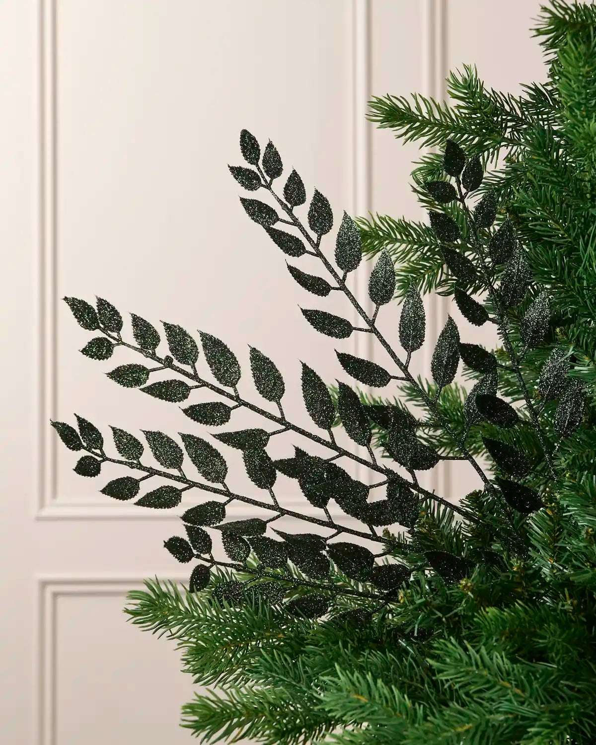 Sage green glitter leaf Christmas tree spray arranged between green Christmas tree branches.