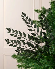 Sage green glitter leaf Christmas tree spray arranged between green Christmas tree branches.