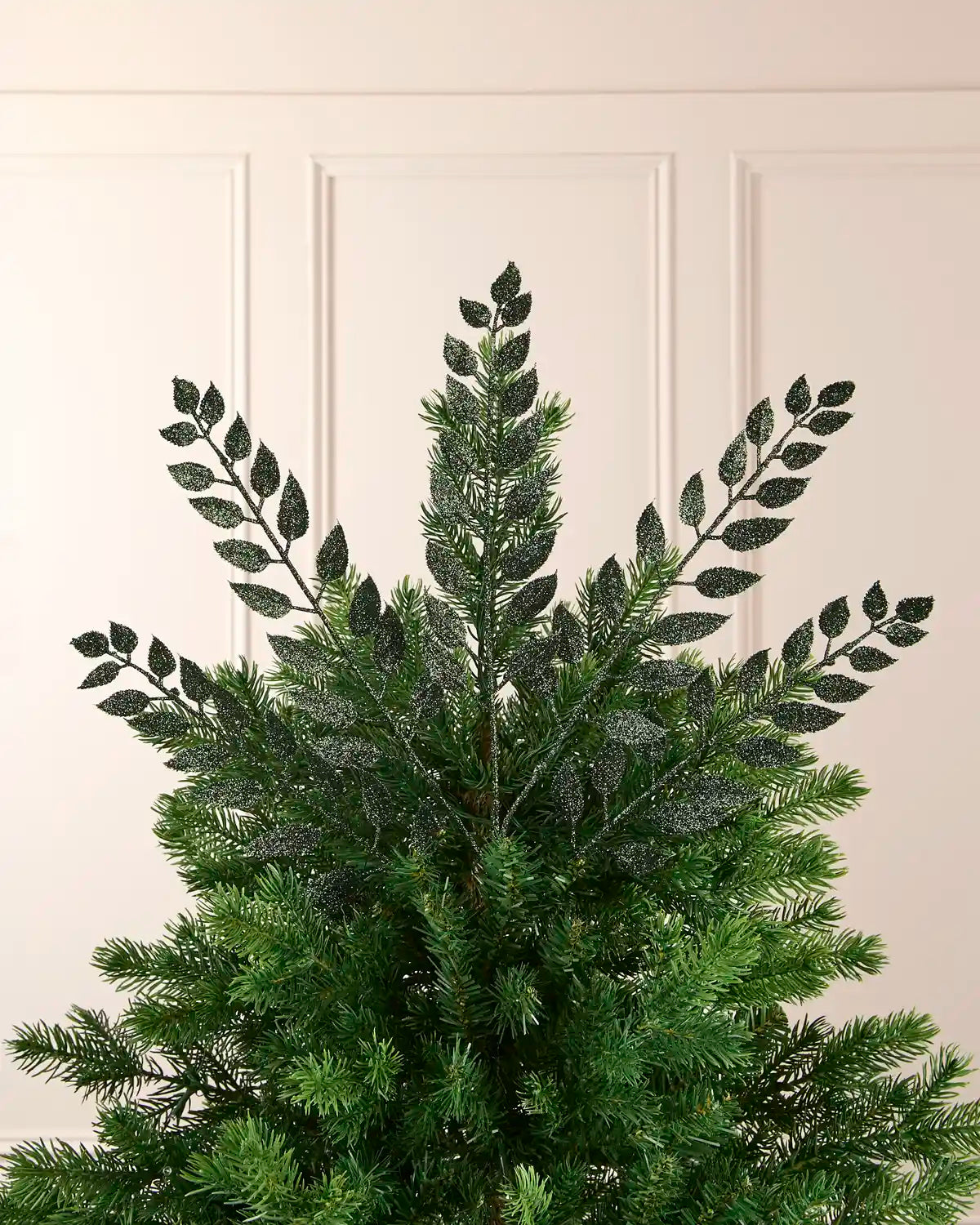 Multiple 73 cm sage green glitter leaf sprays arranged across the top of a Christmas tree.