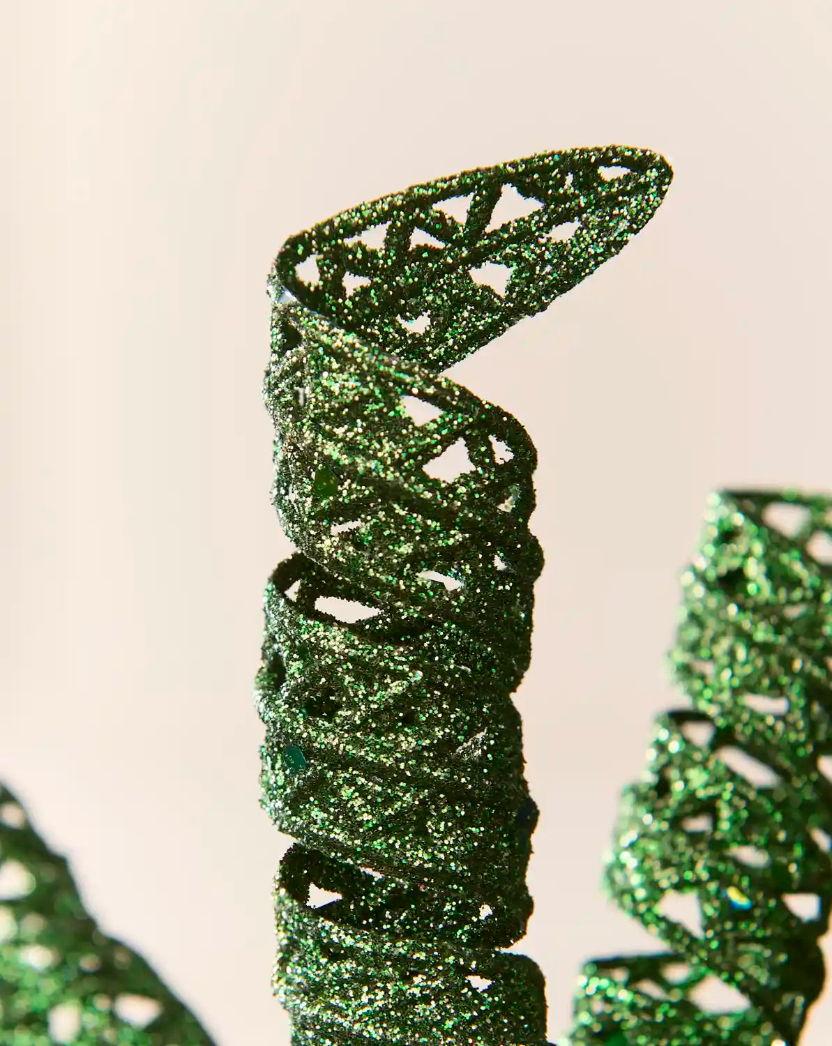 Detailed view of a sage green glitter spiral pick showing its curled shape and textured reflective finish.