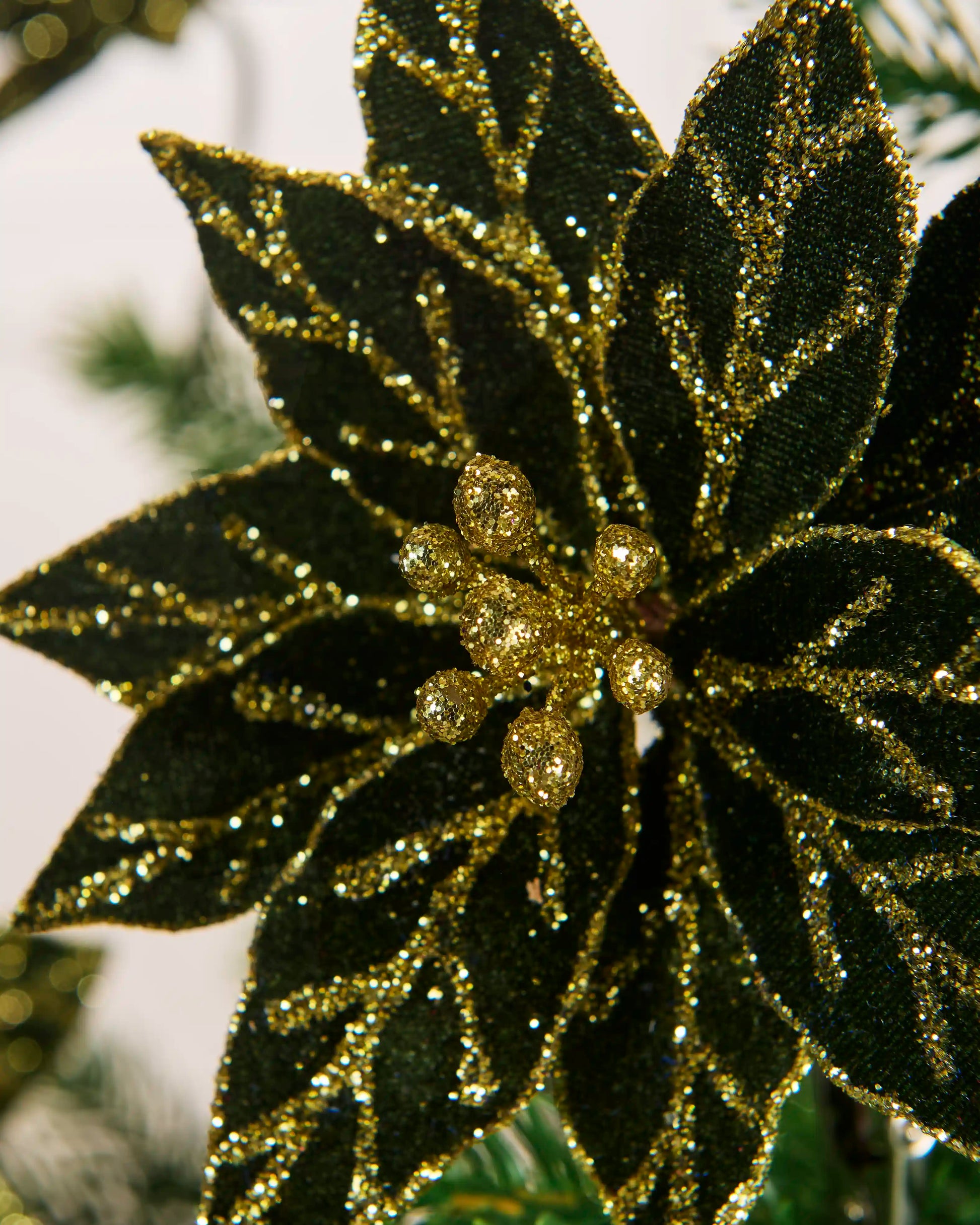 Close-up of the glittered centre and layered sage green leaves of the 15 cm artificial poinsettia.
