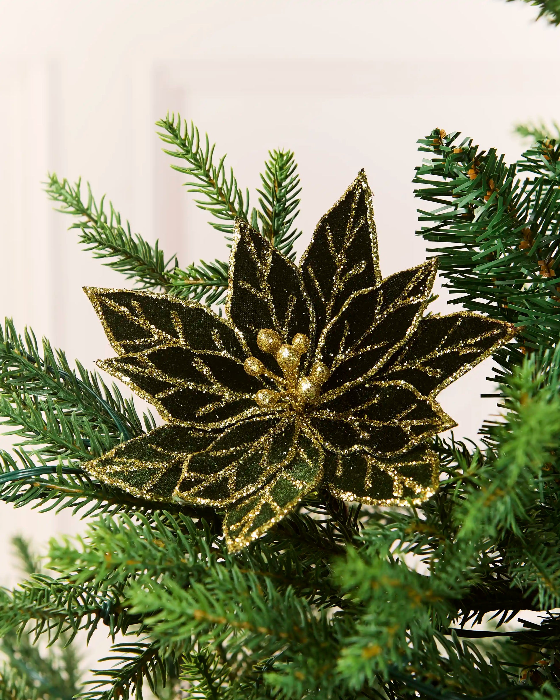 Sage green 15 cm glitter artificial poinsettia clipped among Christmas tree branches.