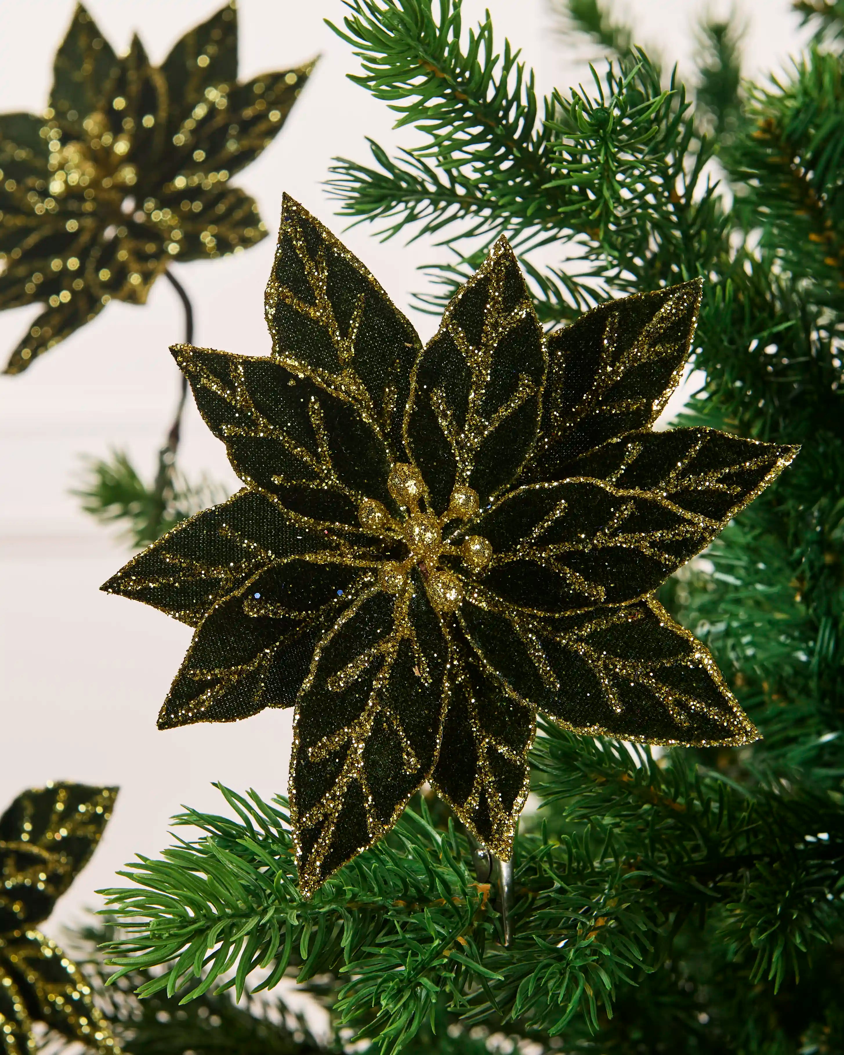 Close-up of a sage green 15 cm artificial poinsettia with layered leaves and gold glitter detailing.