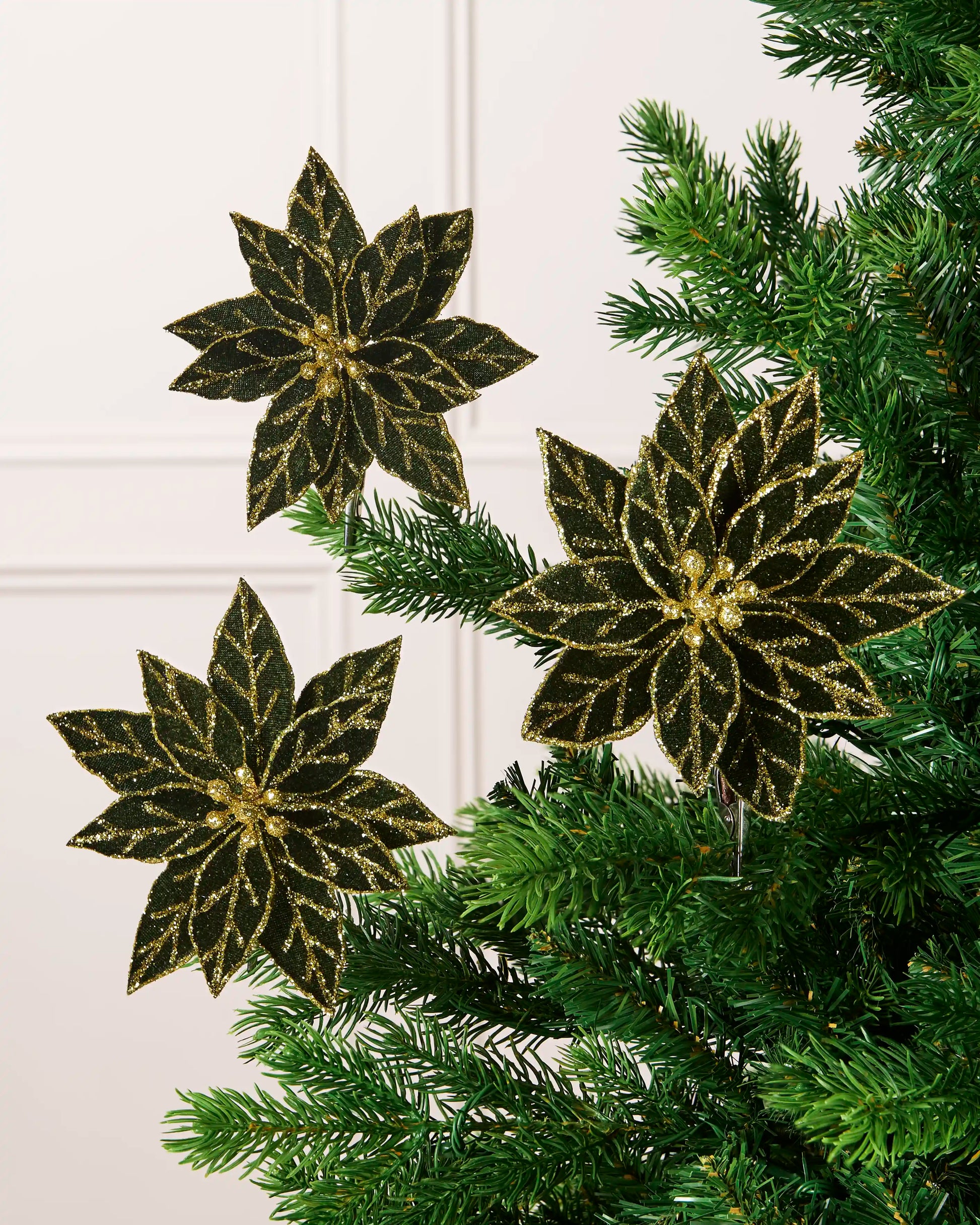 Set of 3 sage green 15 cm artificial poinsettias with gold glitter detailing displayed on a Christmas tree.