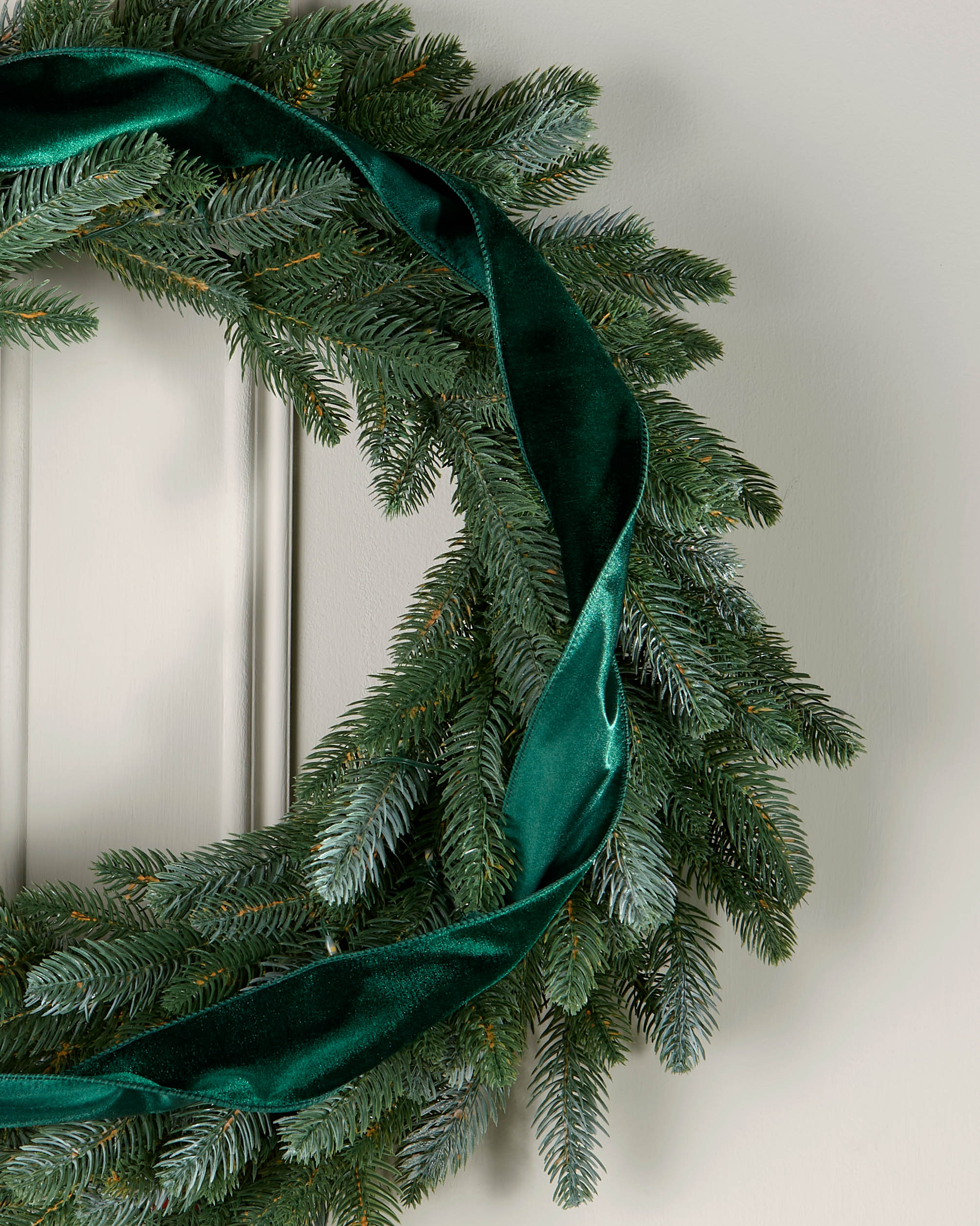 Sage green velvet ribbon styled in a loose spiral on a green Christmas wreath.