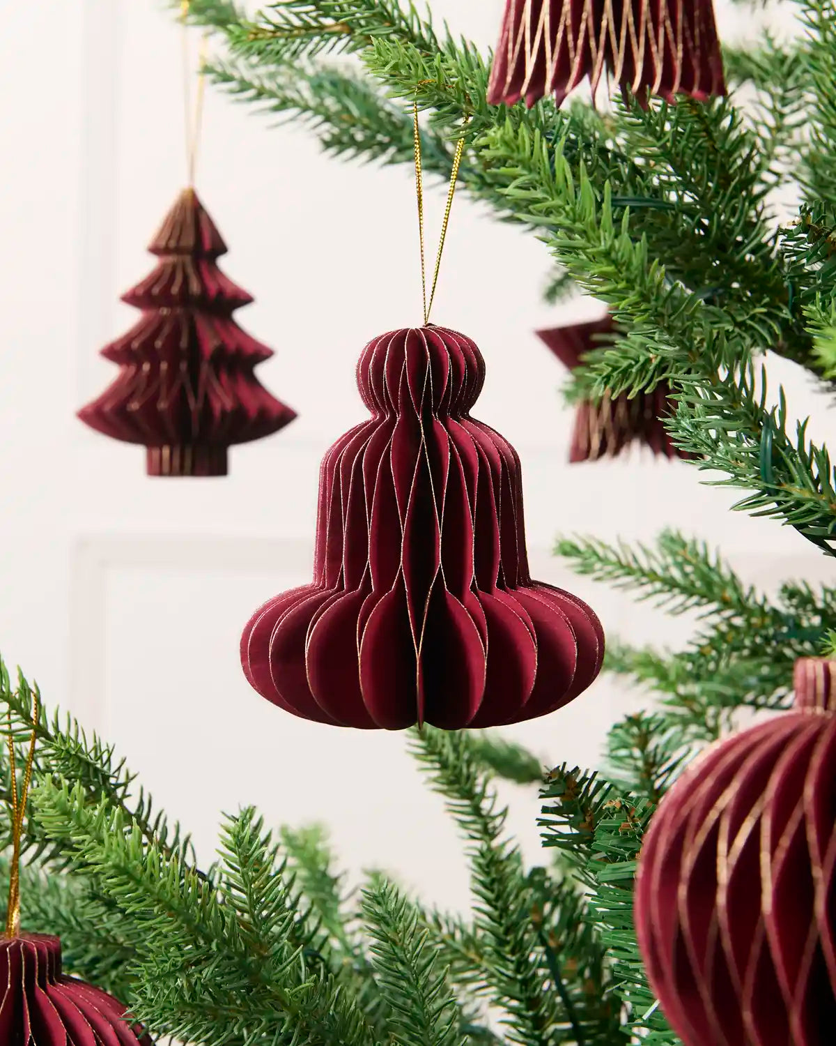 Close-up of a burgundy folded paper bell decoration hanging from a Christmas tree.