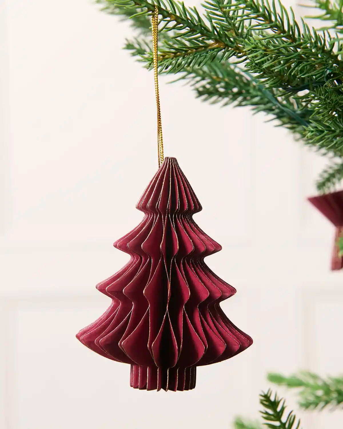 Close-up of a burgundy folded paper Christmas tree decoration with gold glitter edging.