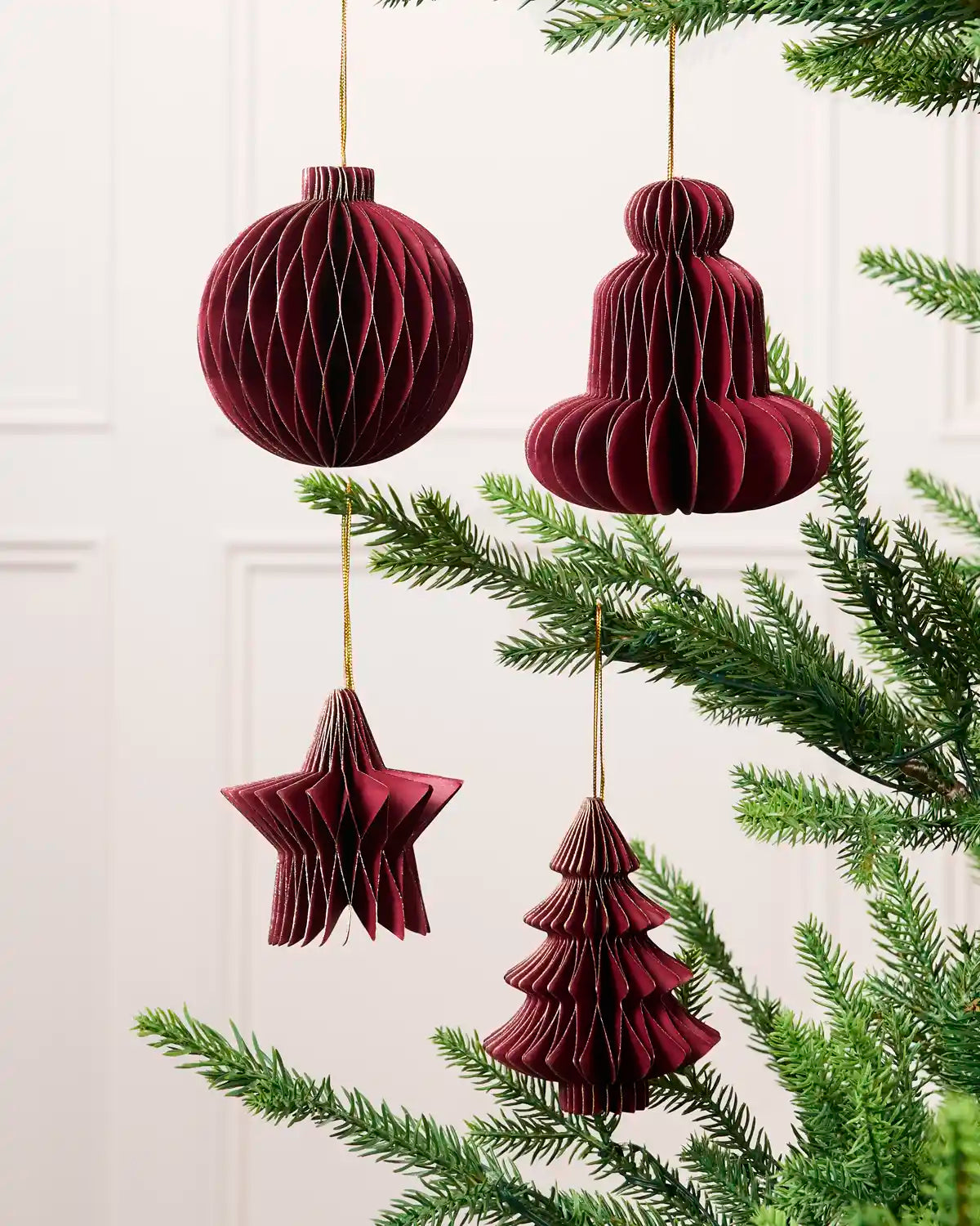 Burgundy paper bauble, bell, star and Christmas tree decorations displayed on a Christmas tree.