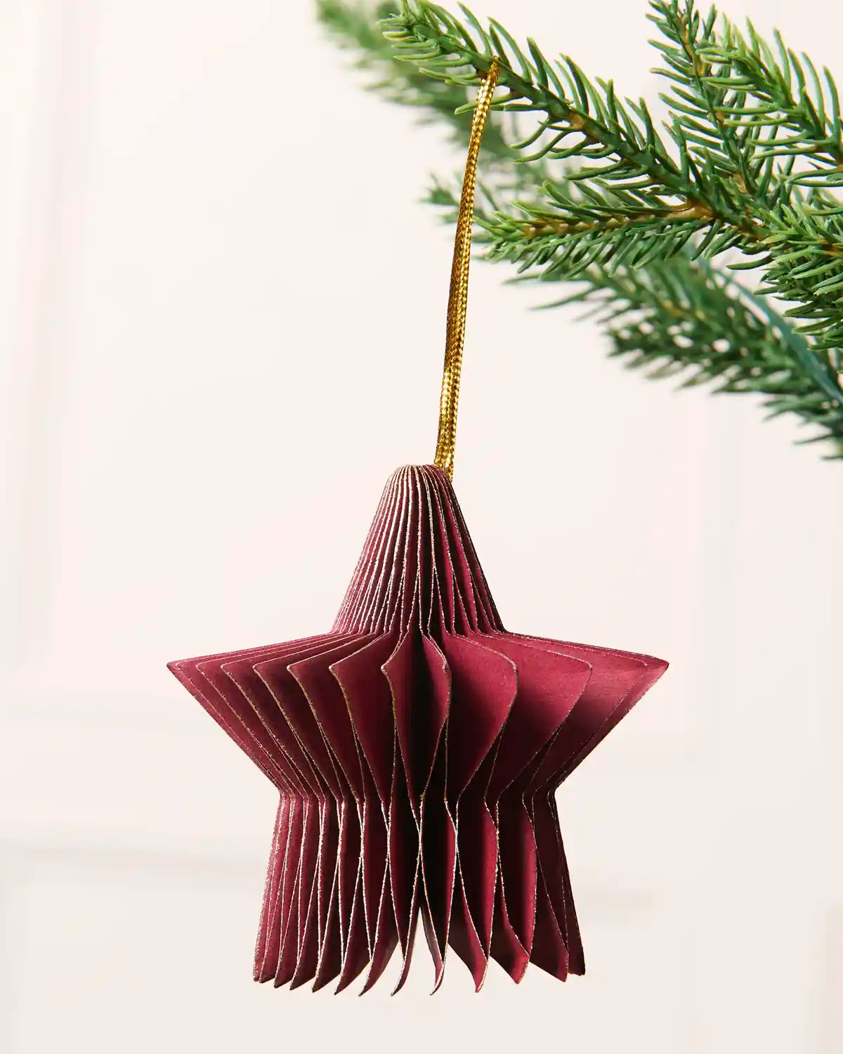 Close-up of a burgundy folded paper star decoration hanging from a Christmas tree.
