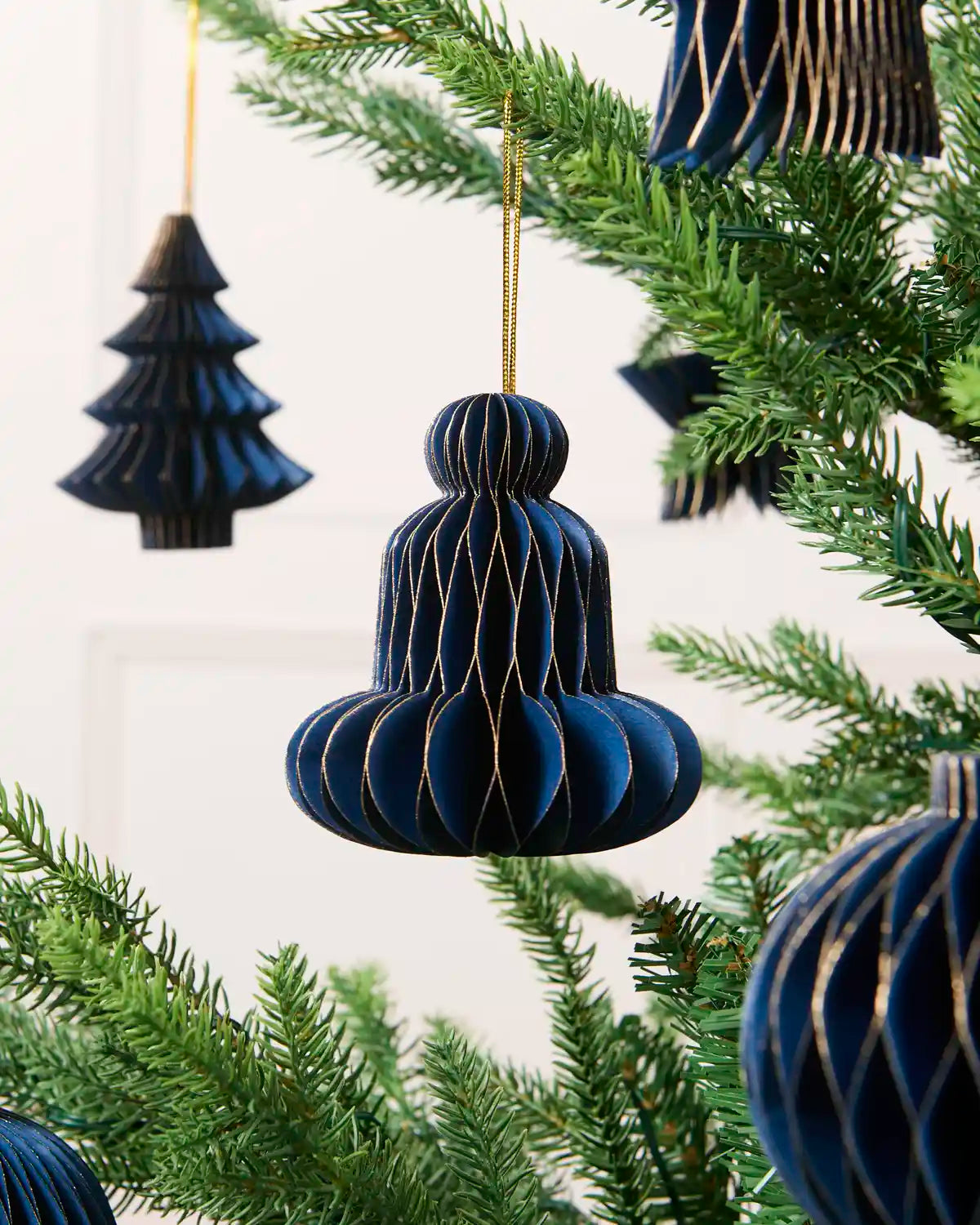 Close-up of a navy folded paper bell decoration hanging from a Christmas tree.