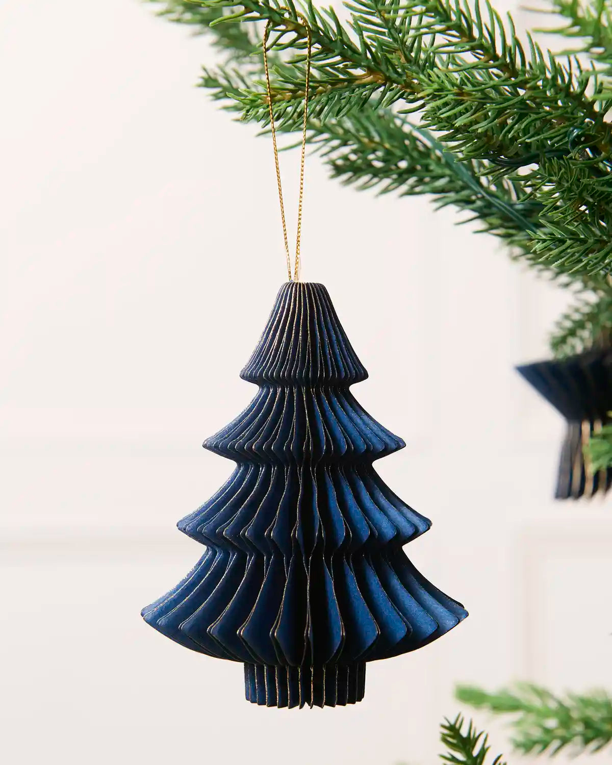 Close-up of a navy folded paper Christmas tree decoration with gold glitter edging.