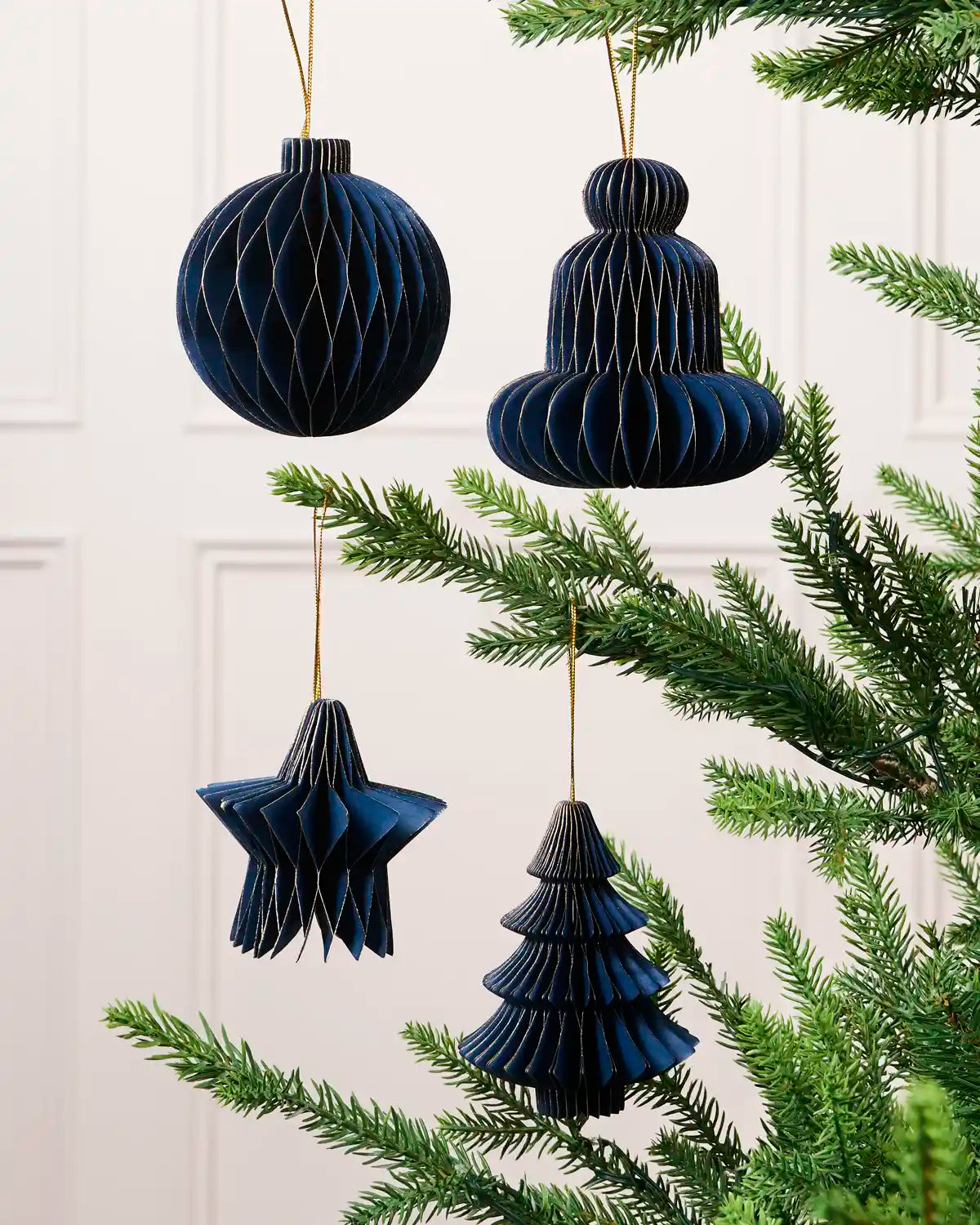 Navy paper bauble, bell, star and Christmas tree decorations displayed on a Christmas tree.